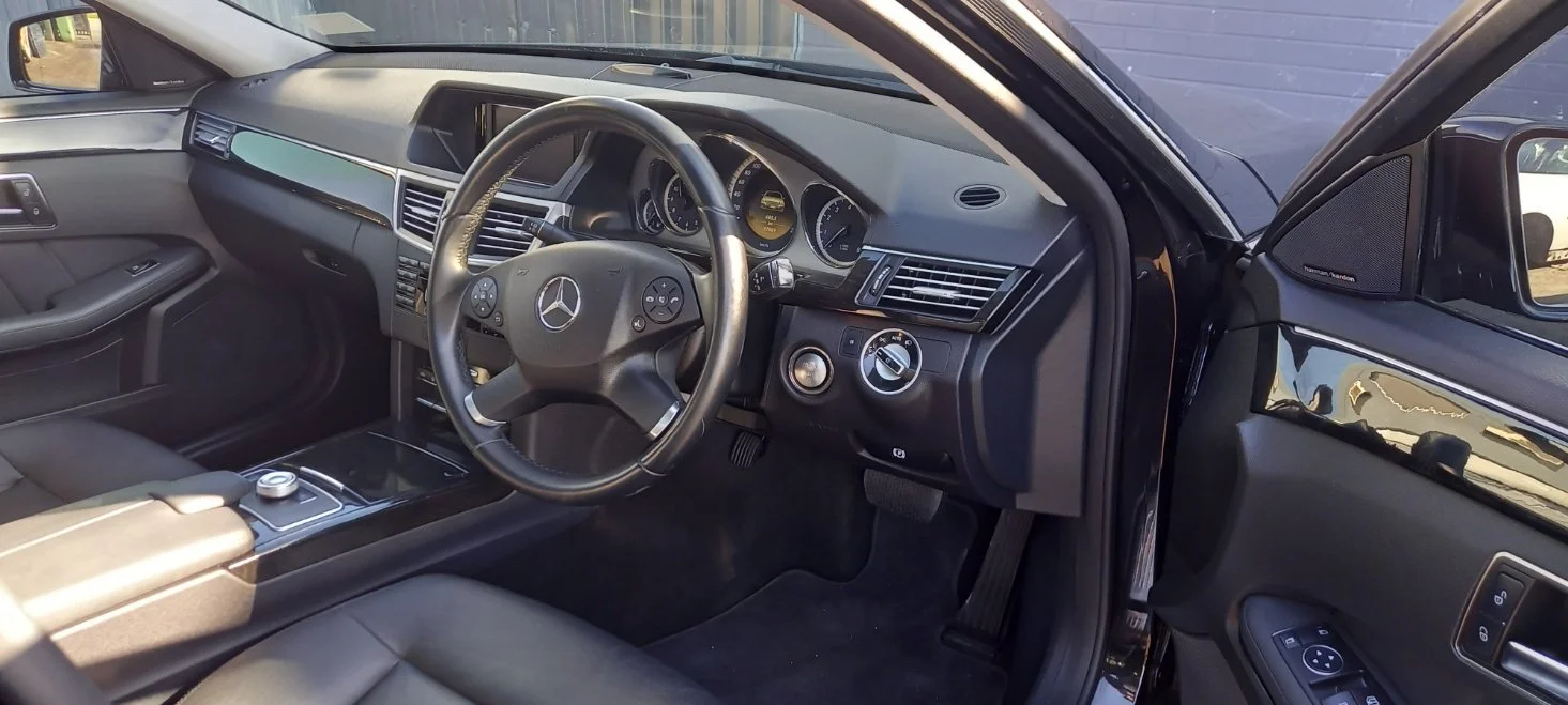 Interior of a Mercedes-Benz vehicle, showing the steering wheel, dashboard, center console, and driver side door with window controls.