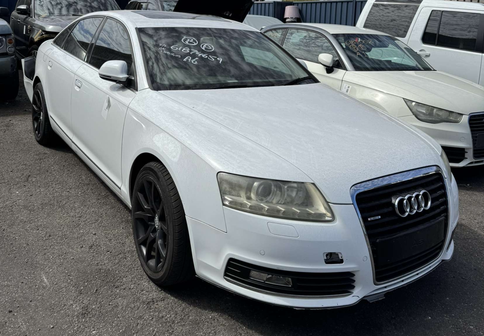 White Audi sedan parked in a lot, with other vehicles nearby.