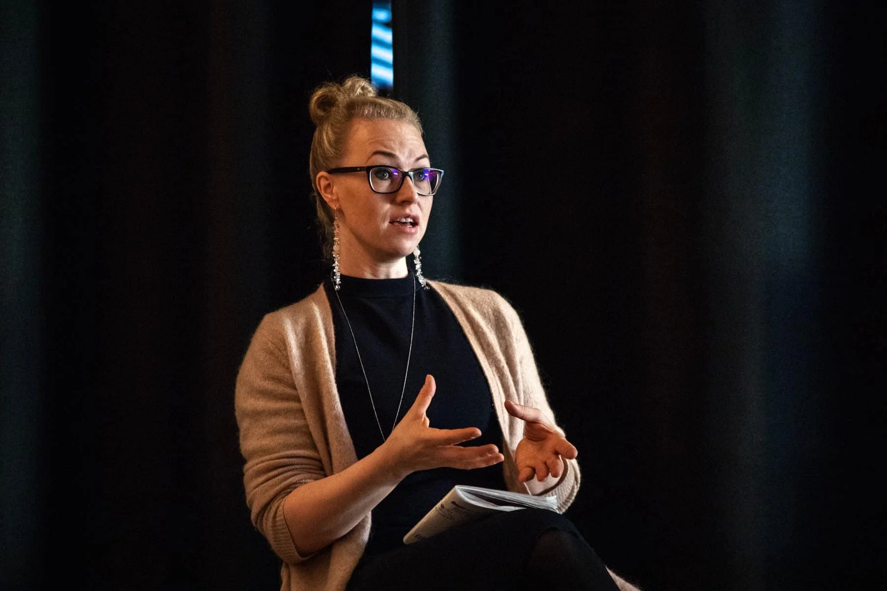 Kaisa Jaakkola puhumassa, hänellä on silmälasit, vaaleat hiukset nutturalla ja vaalea neule.