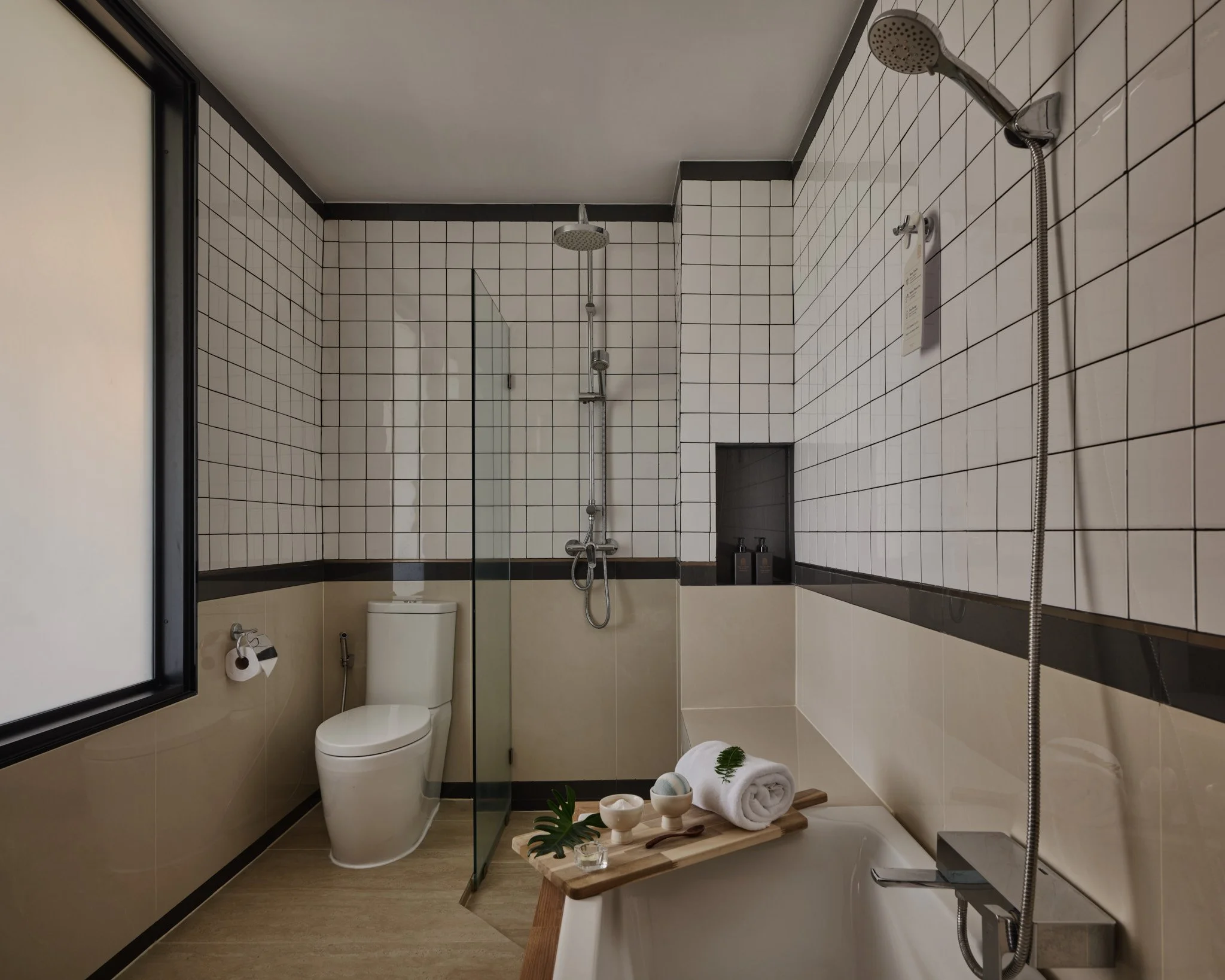 Modern bathroom featuring a shower area with a rain showerhead, a toilet, a bathtub with a rolled towel and toiletries on a wooden tray, a towel, and minimalist decor with wood accents.