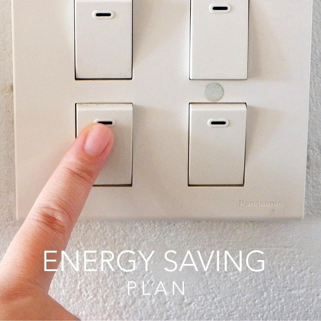 A person's finger is pressing the bottom left switch on a white multi-switch panel, labeled as an energy saving plan.