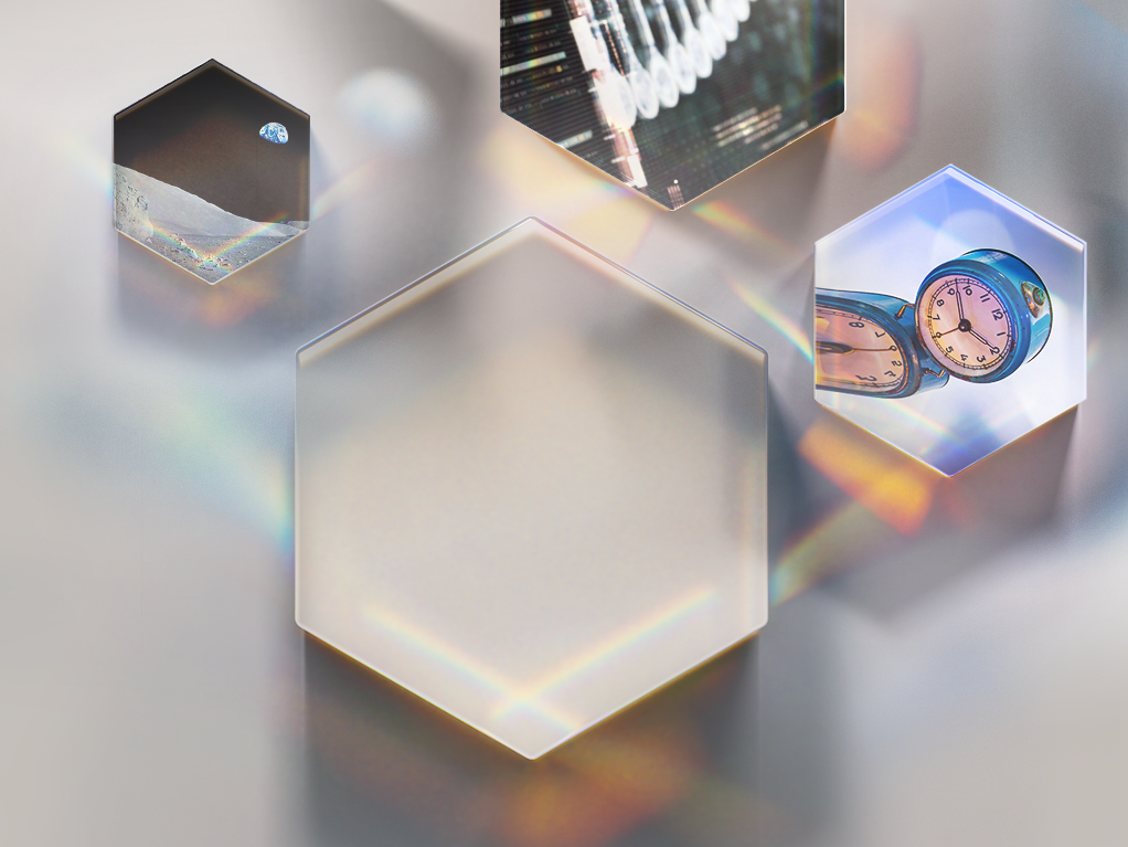 Close-up of four hexagonal glass blocks reflecting light and objects, including a small Earth, a clock, and a digital screen, on a smooth surface.