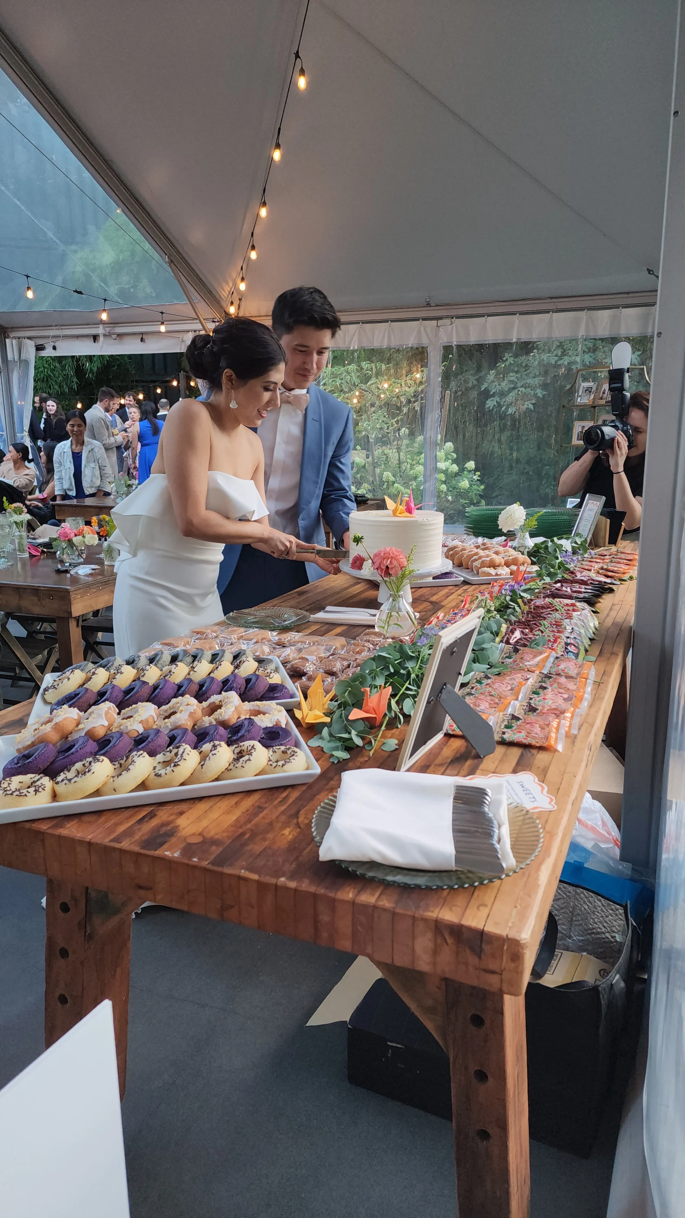 An Asian newly wed couple cutting a wedding cake in front of many Asian snacks