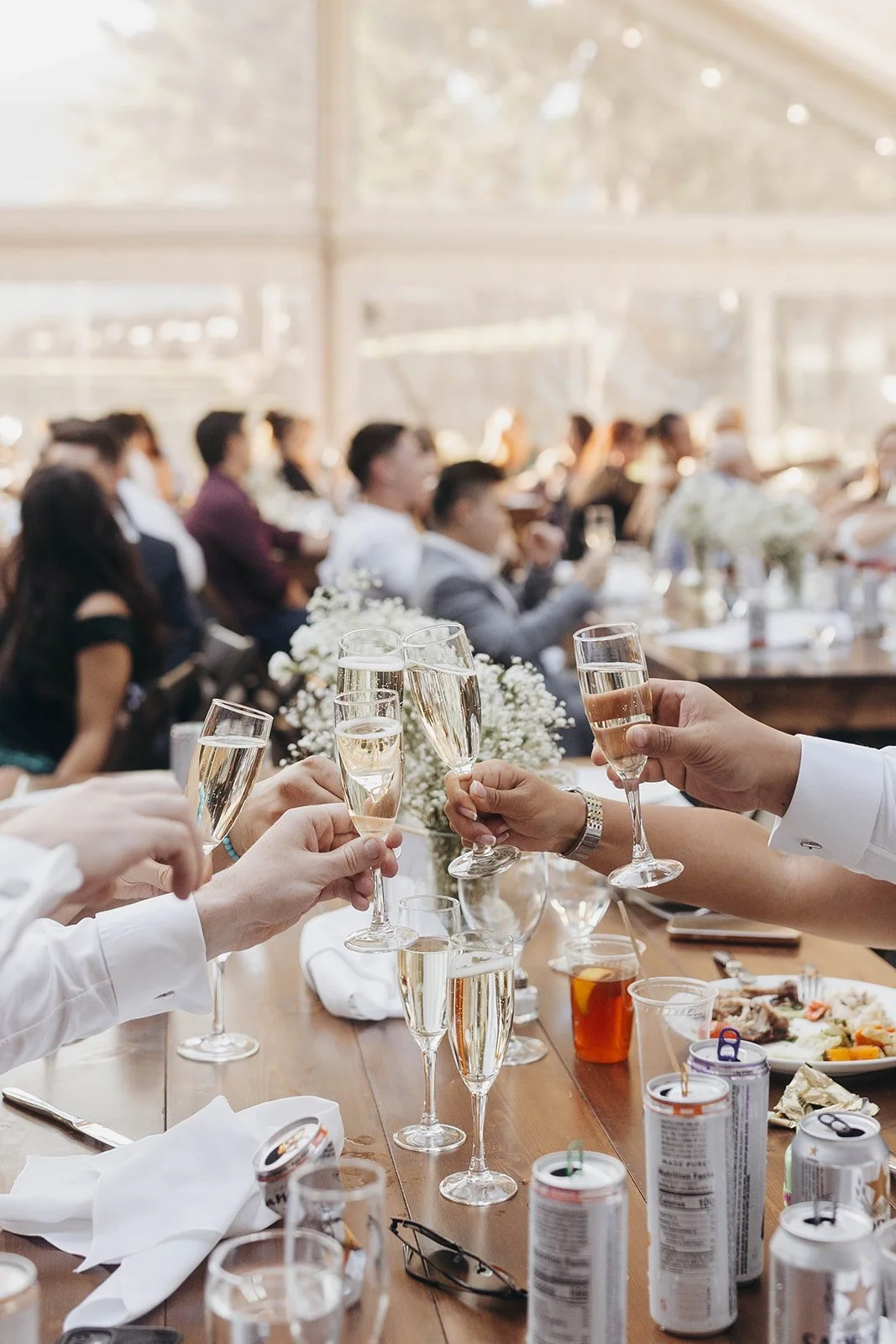 Guests toasting with champagne at a wedding reception, surrounded by tables with drinks and flowers.