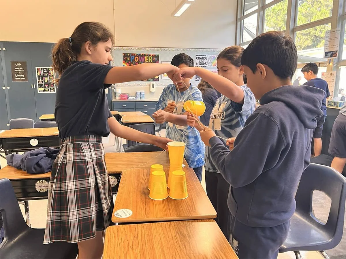 Middle school students collaborating on a teamwork challenge using cups and string.