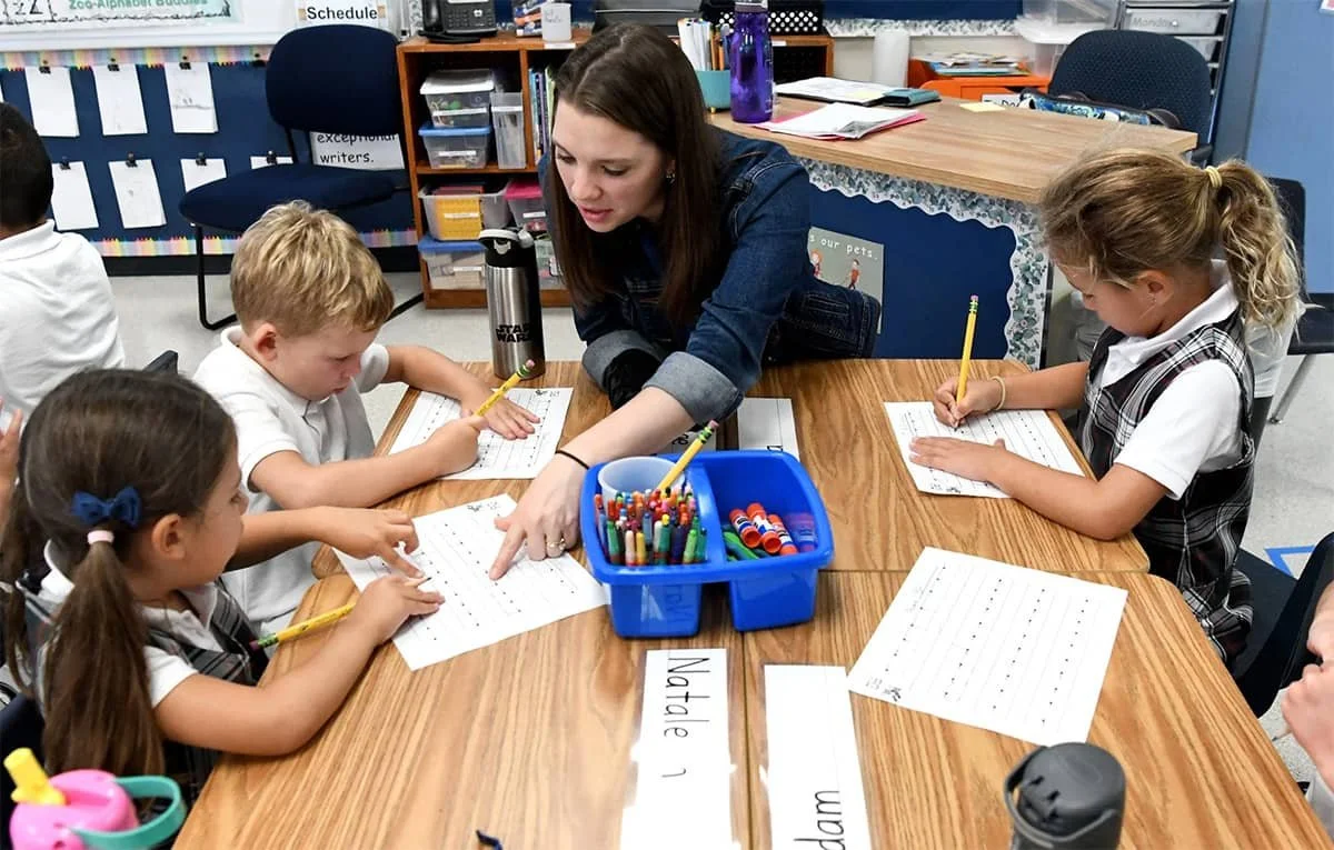 Teacher guiding a small group of kindergarten students as they practice handwriting.