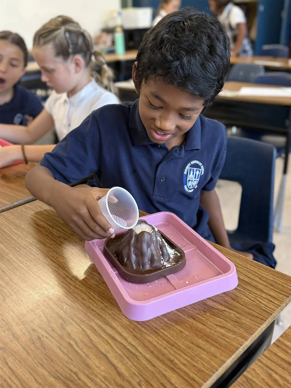 Student pouring liquid onto a model volcano during a hands-on science activity.