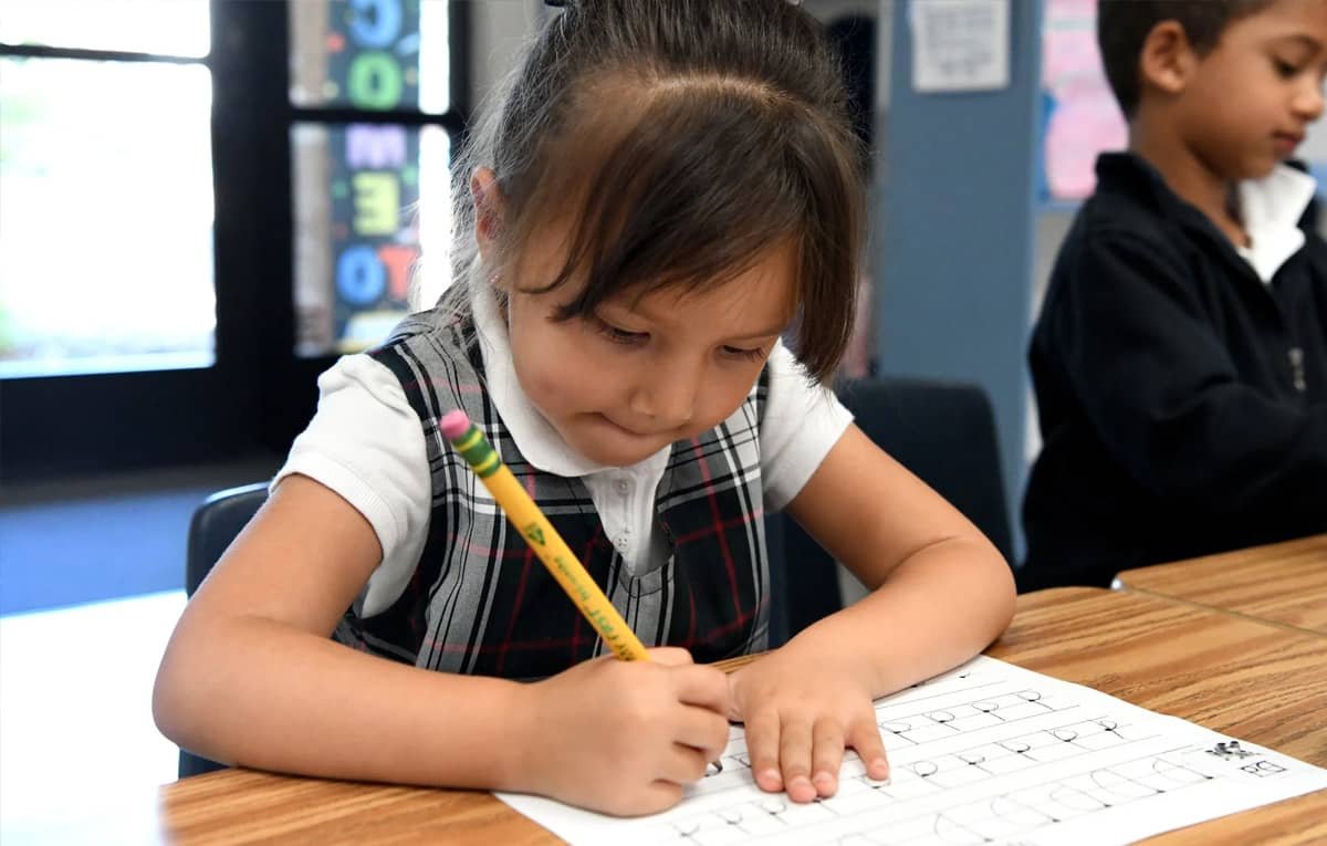 Elementary student concentrating while practicing handwriting at her desk.