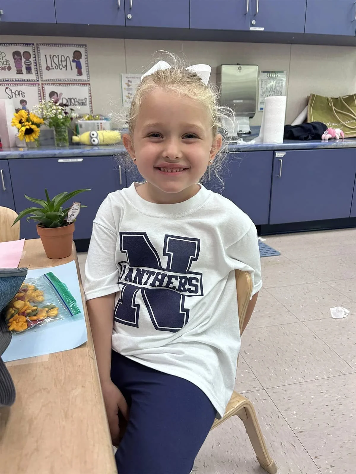 Student smiling while sitting at a classroom table wearing a Panthers shirt.