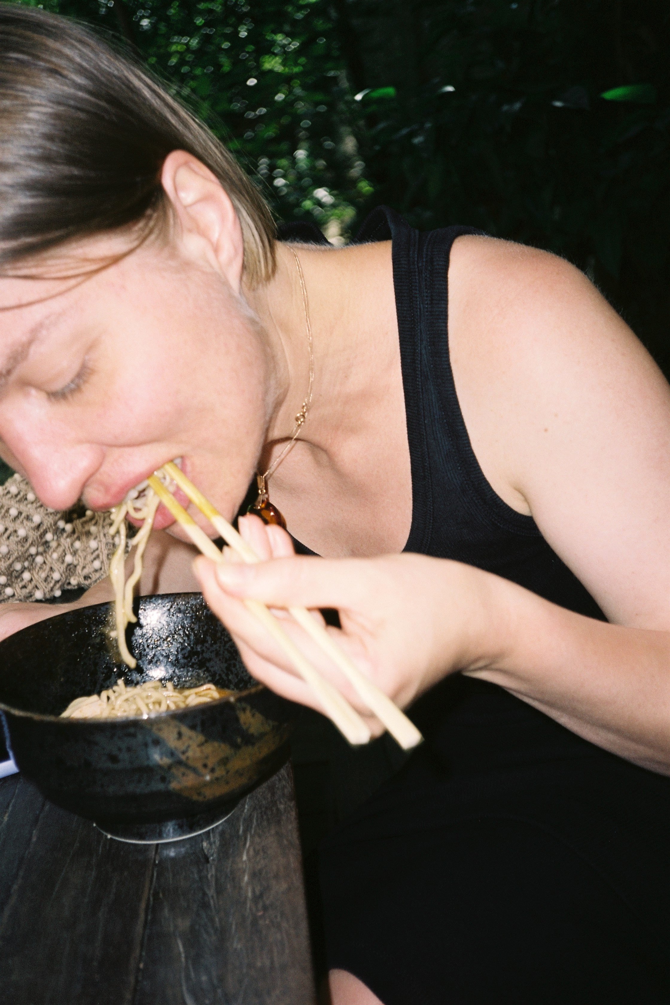 Une jeune femme qui mange des nouilles dans un bol dans un restaurant sombre