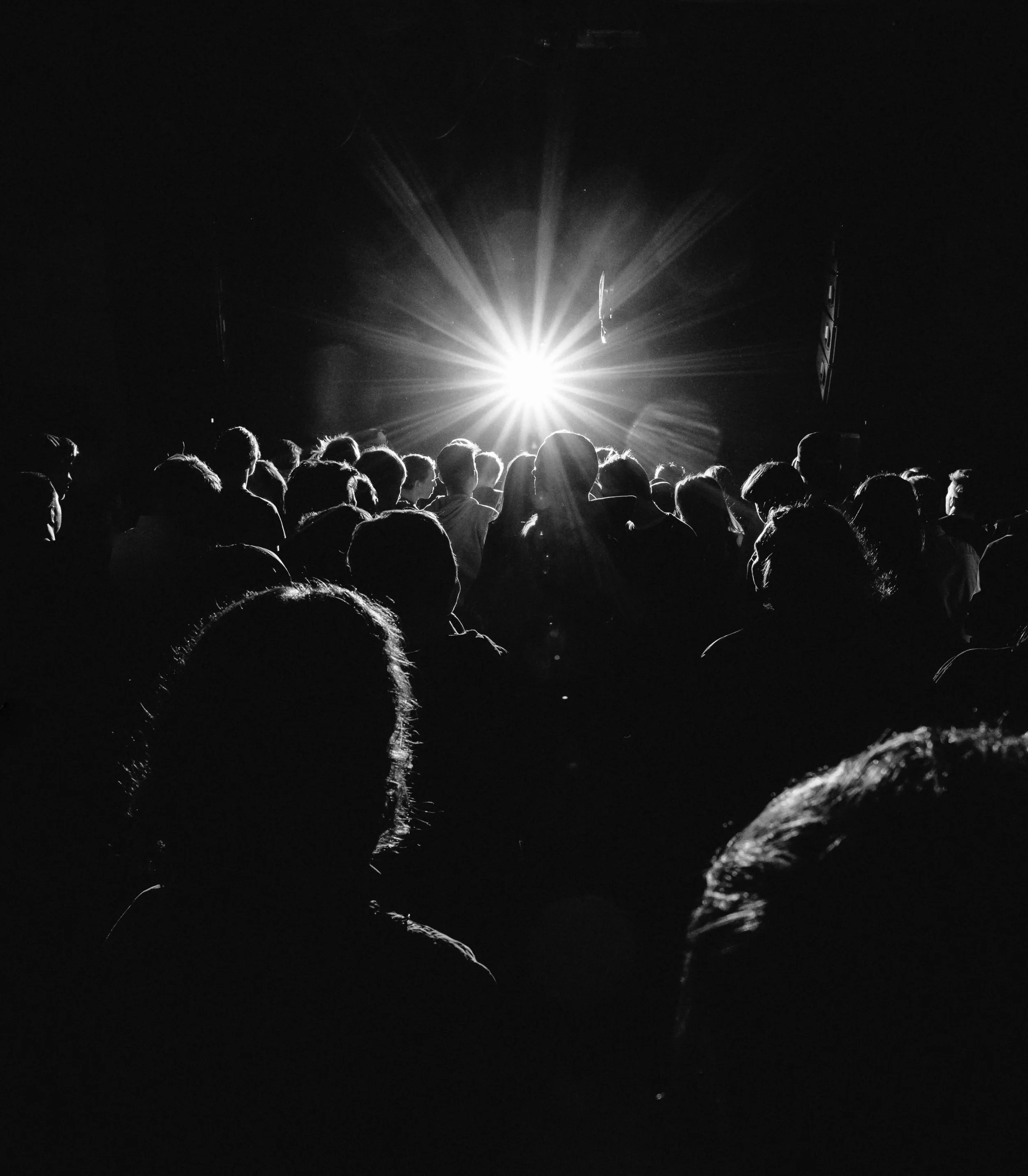 Vue arrière d’une immense foule de personnes qui dansent lors d’une fête dans un endroit sombre éclairé par un projecteur lumineux