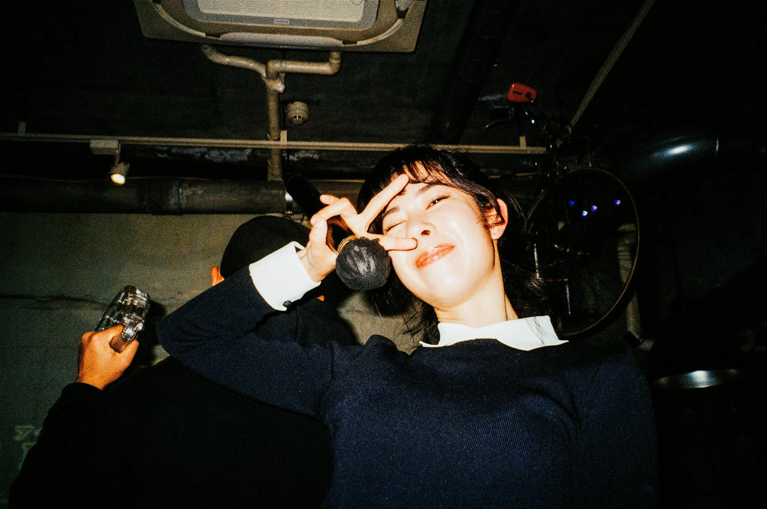 Une jeune femme sourit à l’appareil photo et fait le signe de la paix devant son visage.