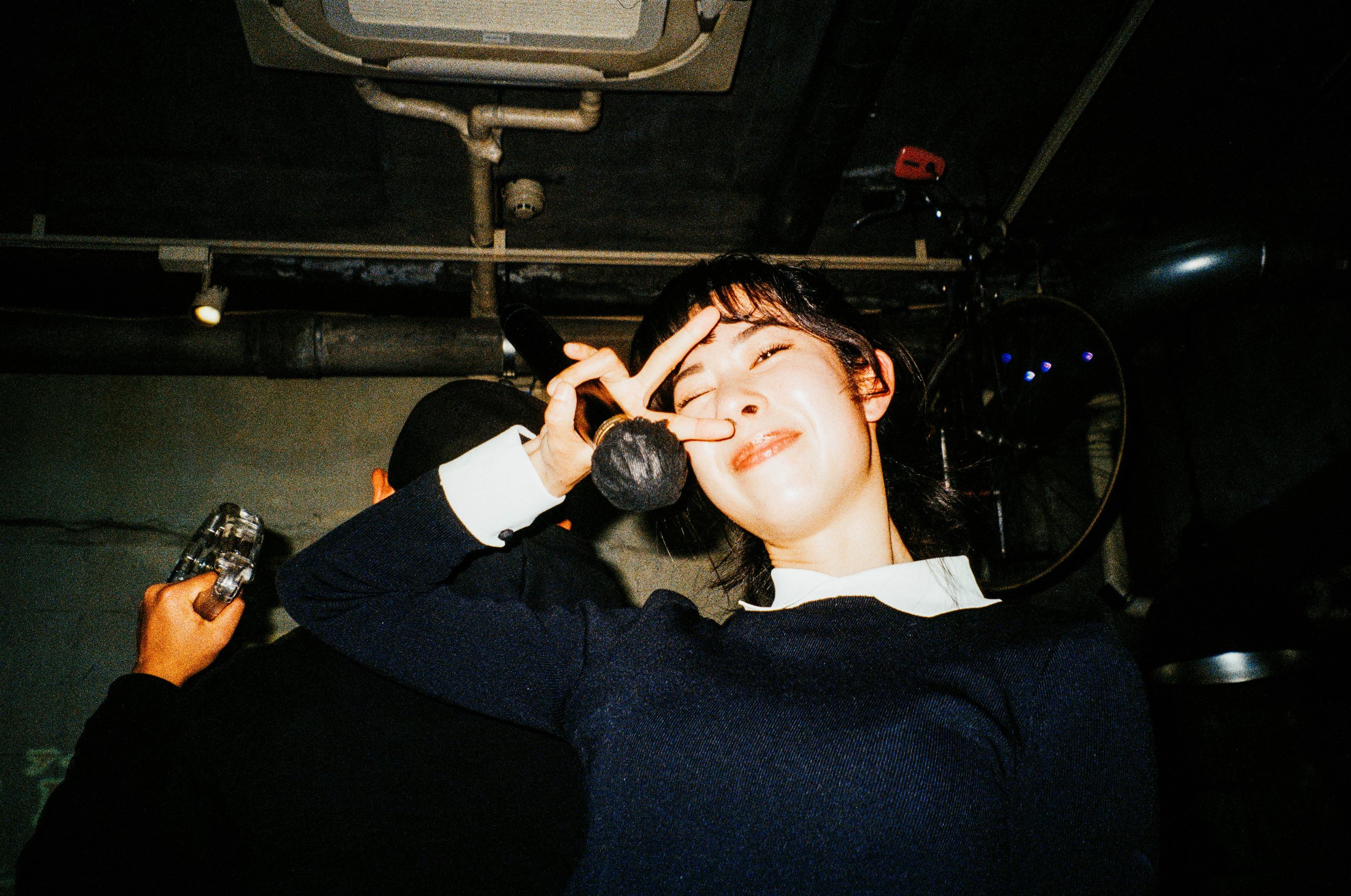 Eine junge Frau lächelt in die Kamera und macht ein Peace-Zeichen vor dem Gesicht.