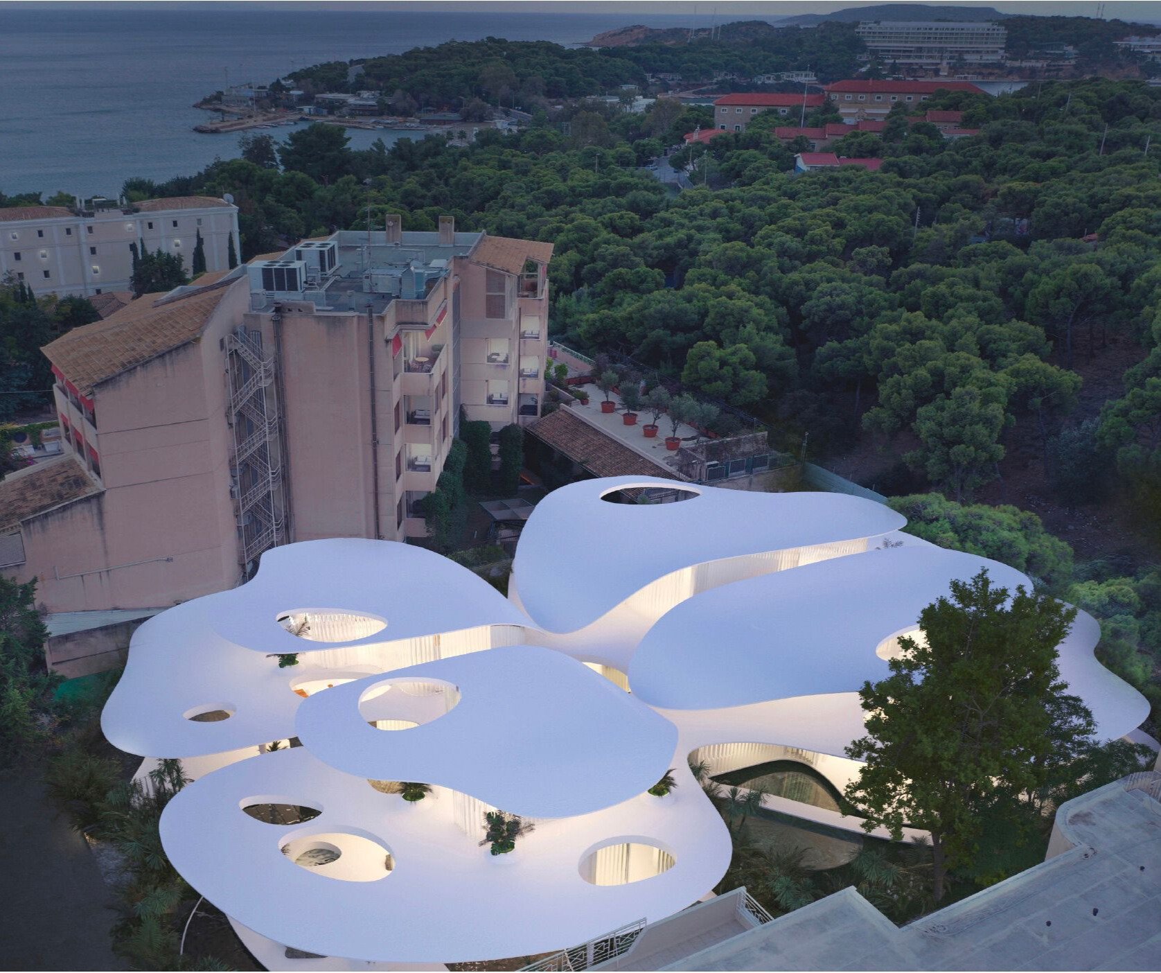 Aerial view of a modern, white architectural building with organic, flowing shapes and circular cutouts, situated among trees and next to older, traditional buildings near a body of water.