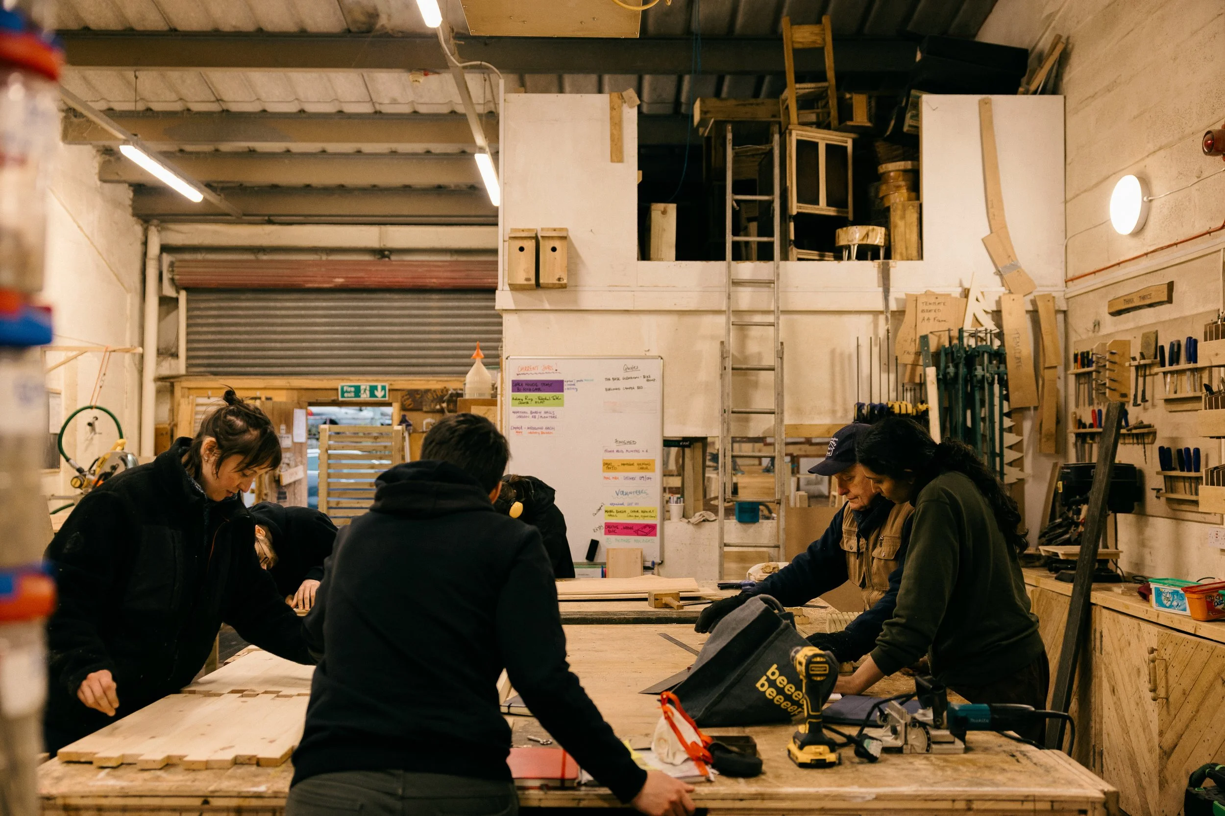 A group of people working in a woodworking workshop, engaged in building projects with wood and tools.