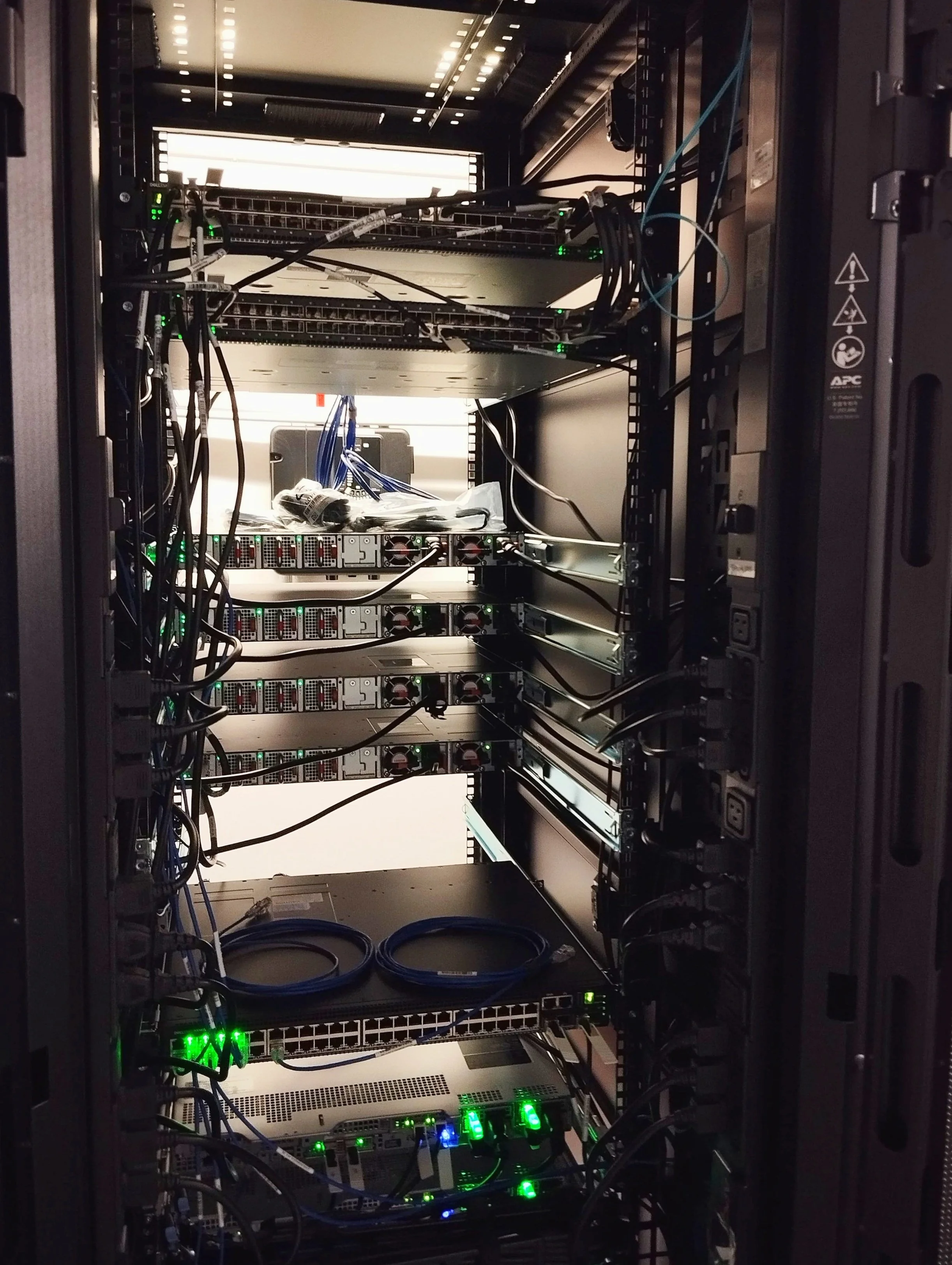 Armadio rack con server, switch e apparecchiature informatiche, cavi e luci LED verdi.