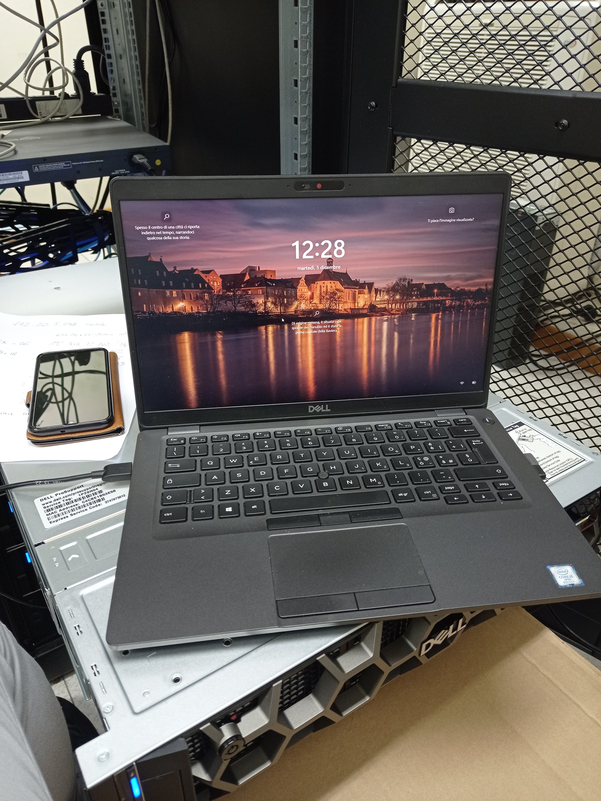 Laptop aperto su un server in una sala dati, con uno smartphone accanto. Con il tecnico in presenza.