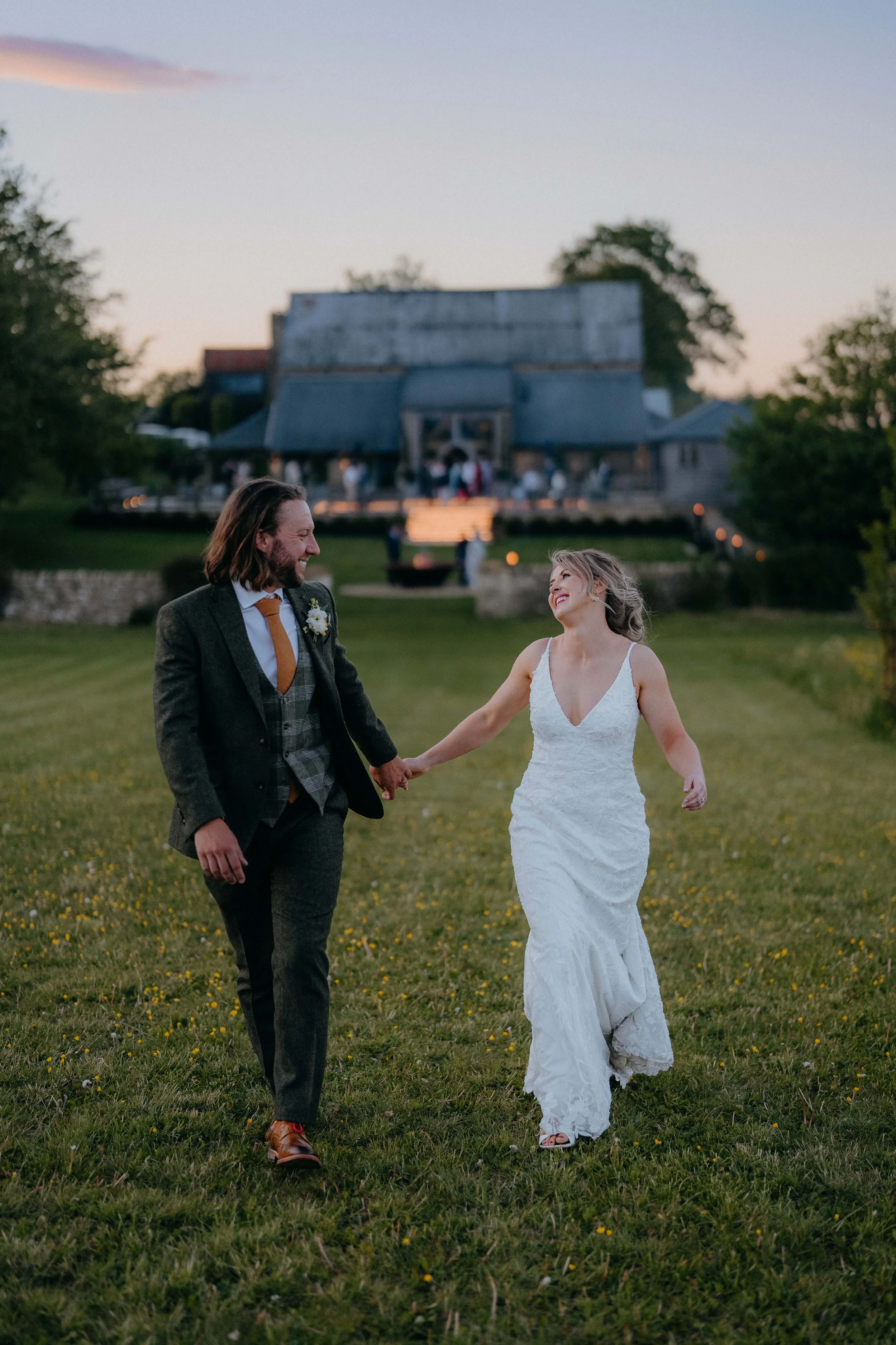 A bride and groom holding hands and smiling at each other outdoors during their wedding at sunset.