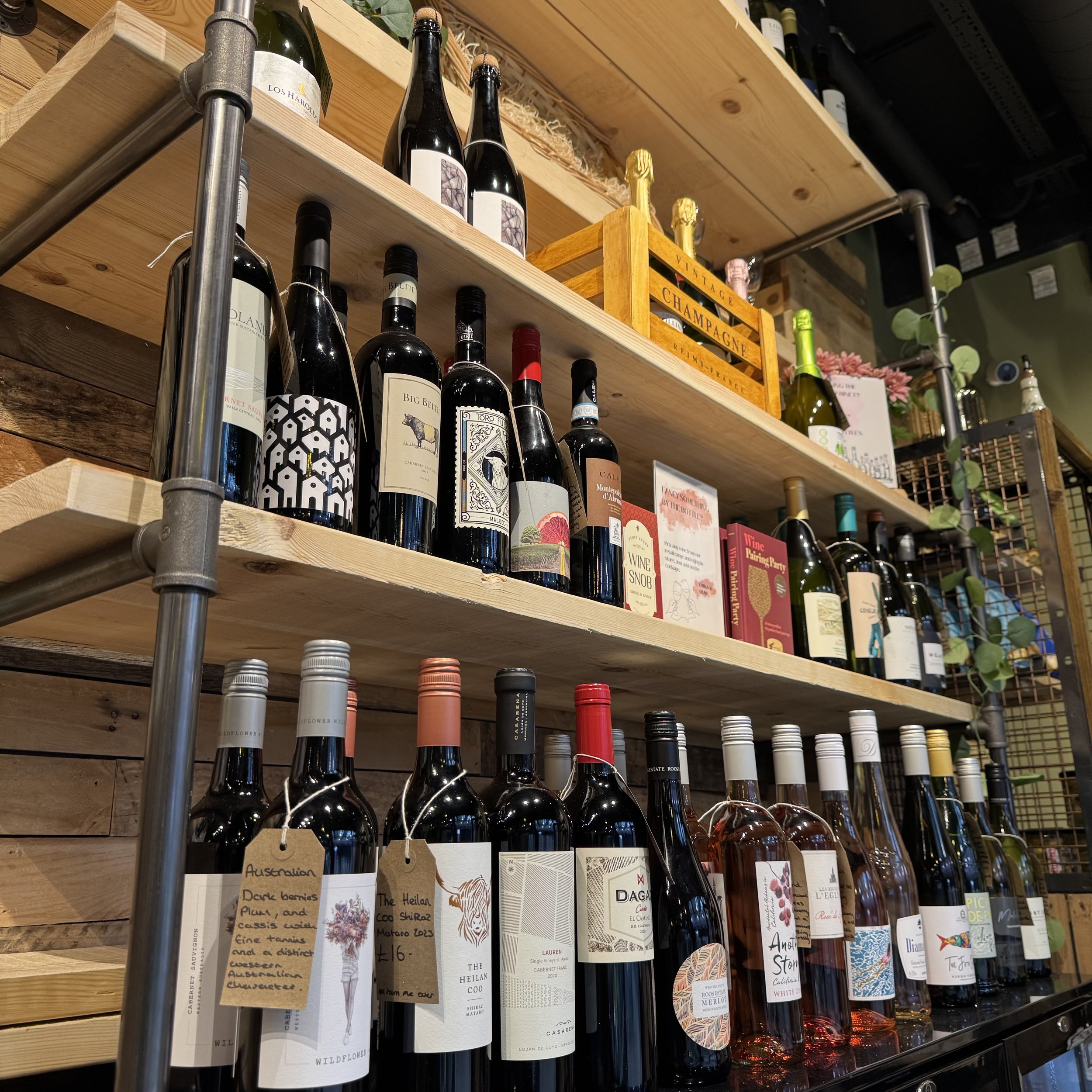 Shelves displaying various bottles of wine and champagne, arranged neatly with some labels visible. There are also books and decorative items, including a wooden box labeled "Champagne." The atmosphere gives a rustic, organized appearance.