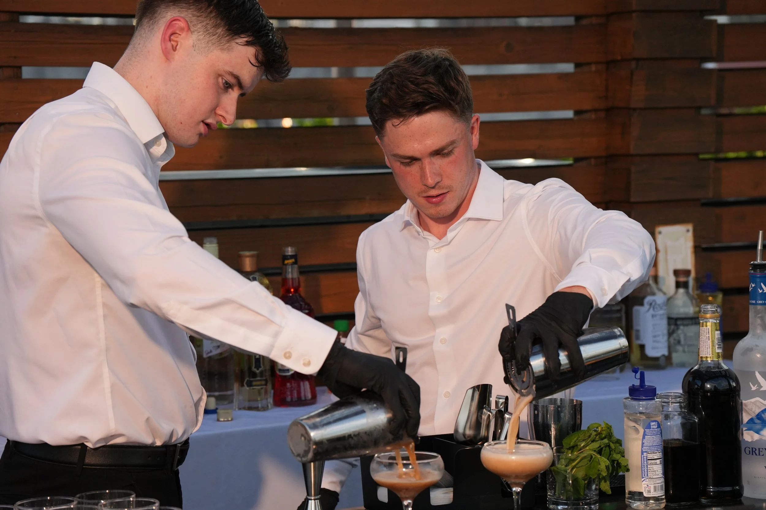 Two bartenders pouring a martini into a glass