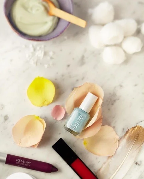 Nail polish bottles, makeup cotton balls, and rose petals on a marble surface.