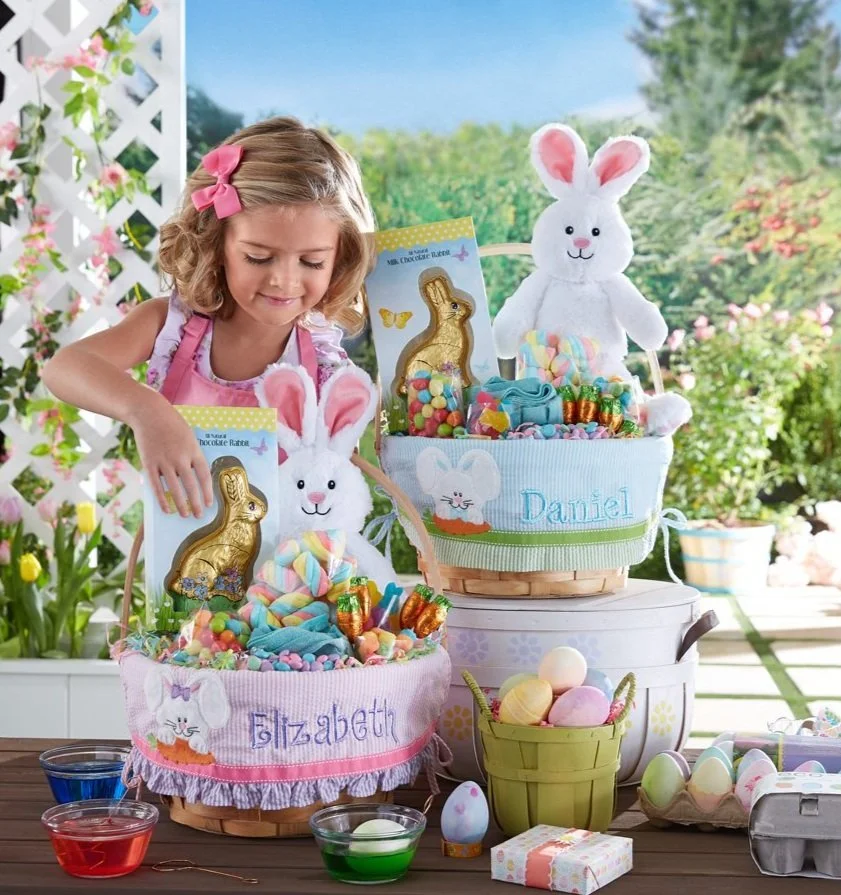 A young girl arranging Easter baskets filled with candy, decorated with plush bunny toys, and colorful eggs outdoors during spring.