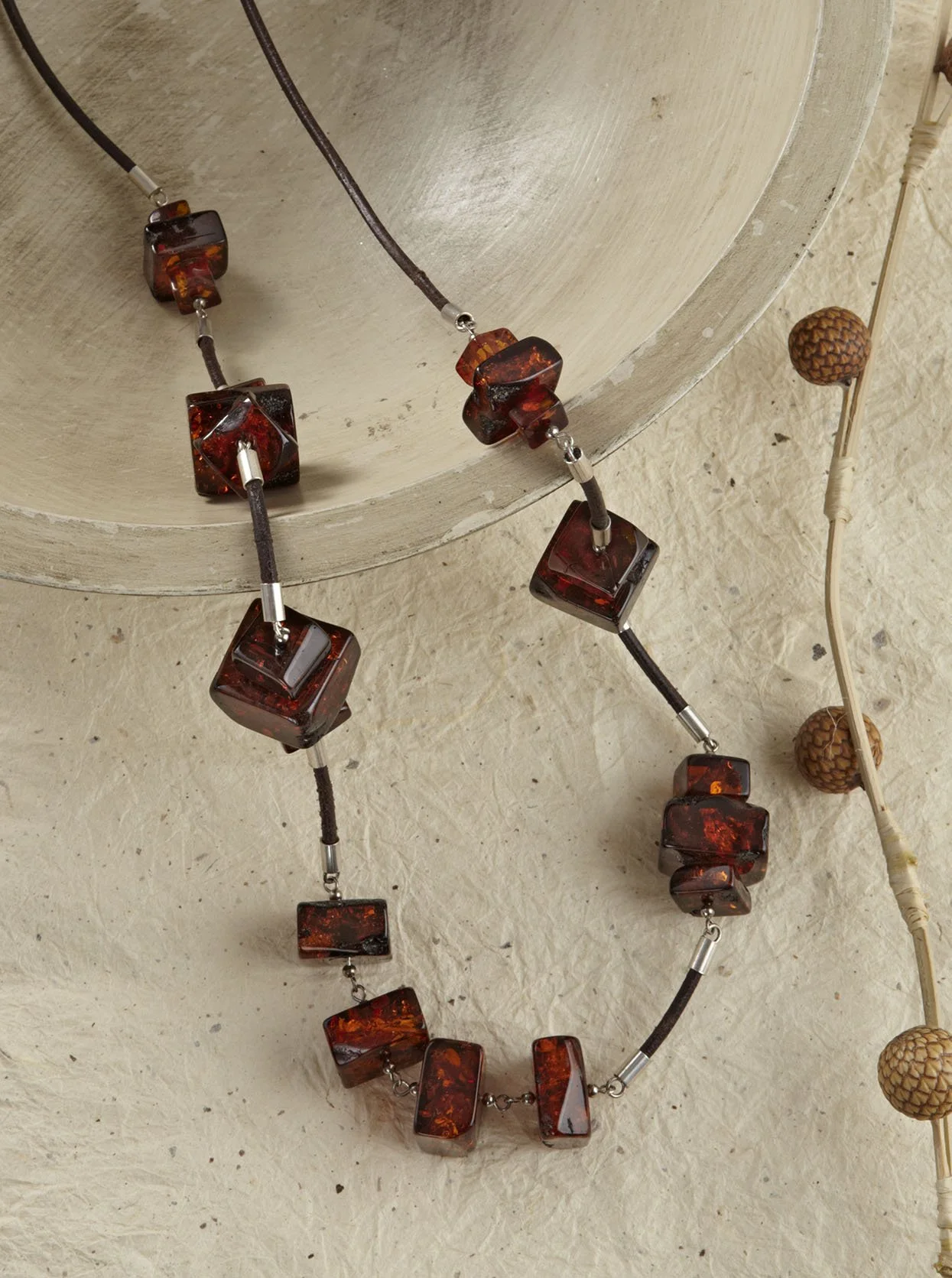 A necklace with rectangular amber-colored beads, laid on a textured beige surface next to a string of decorative balls.