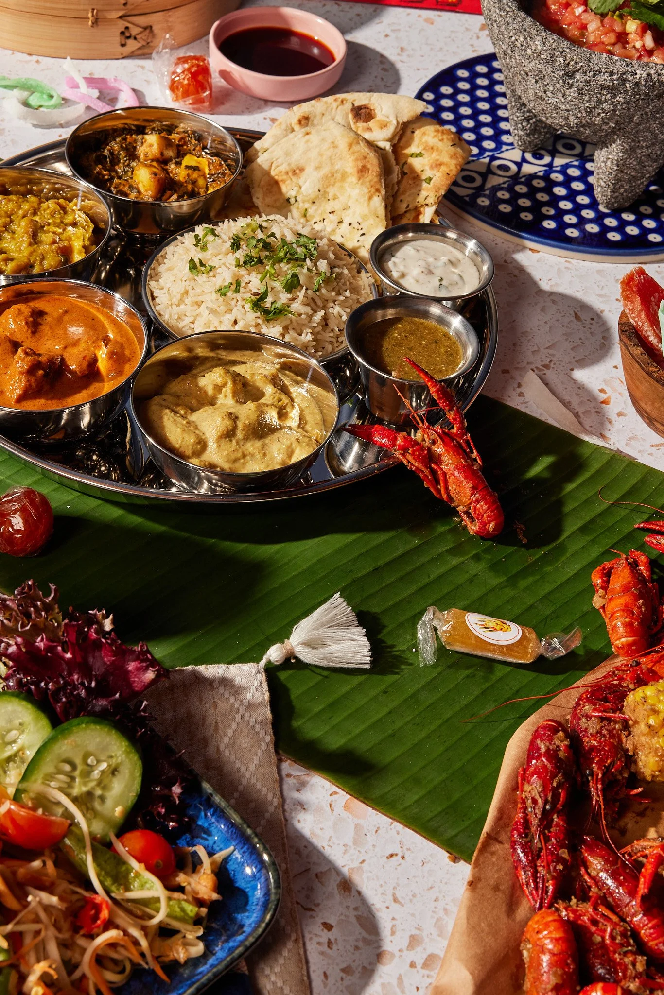 An assortment of Indian dishes, including various curries, rice, naan bread, and lobster, is displayed on a table with toppings and sides.
