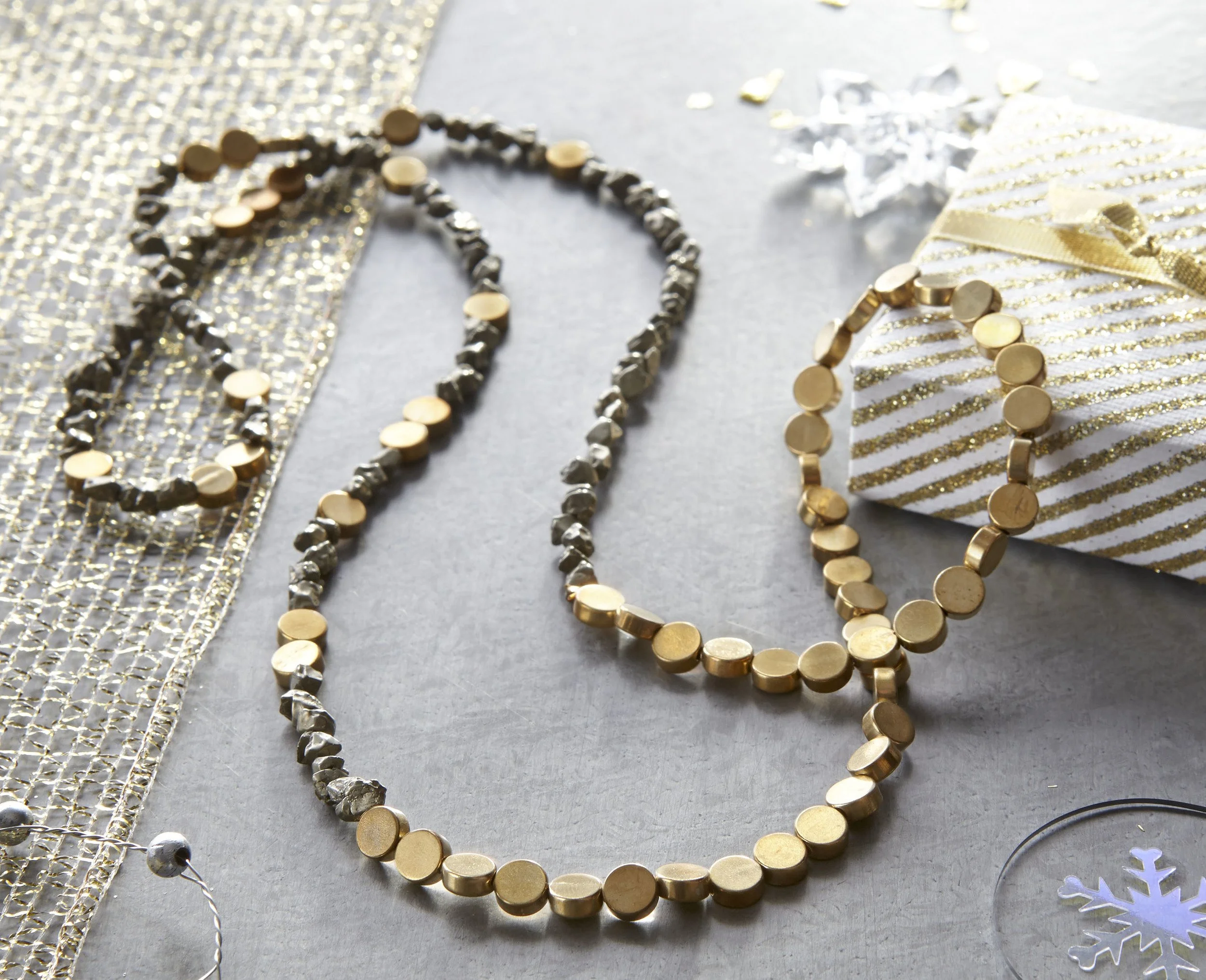 Gold and silver necklaces arranged on a Christmas-themed surface with a white and gold gift box and holiday decorations.