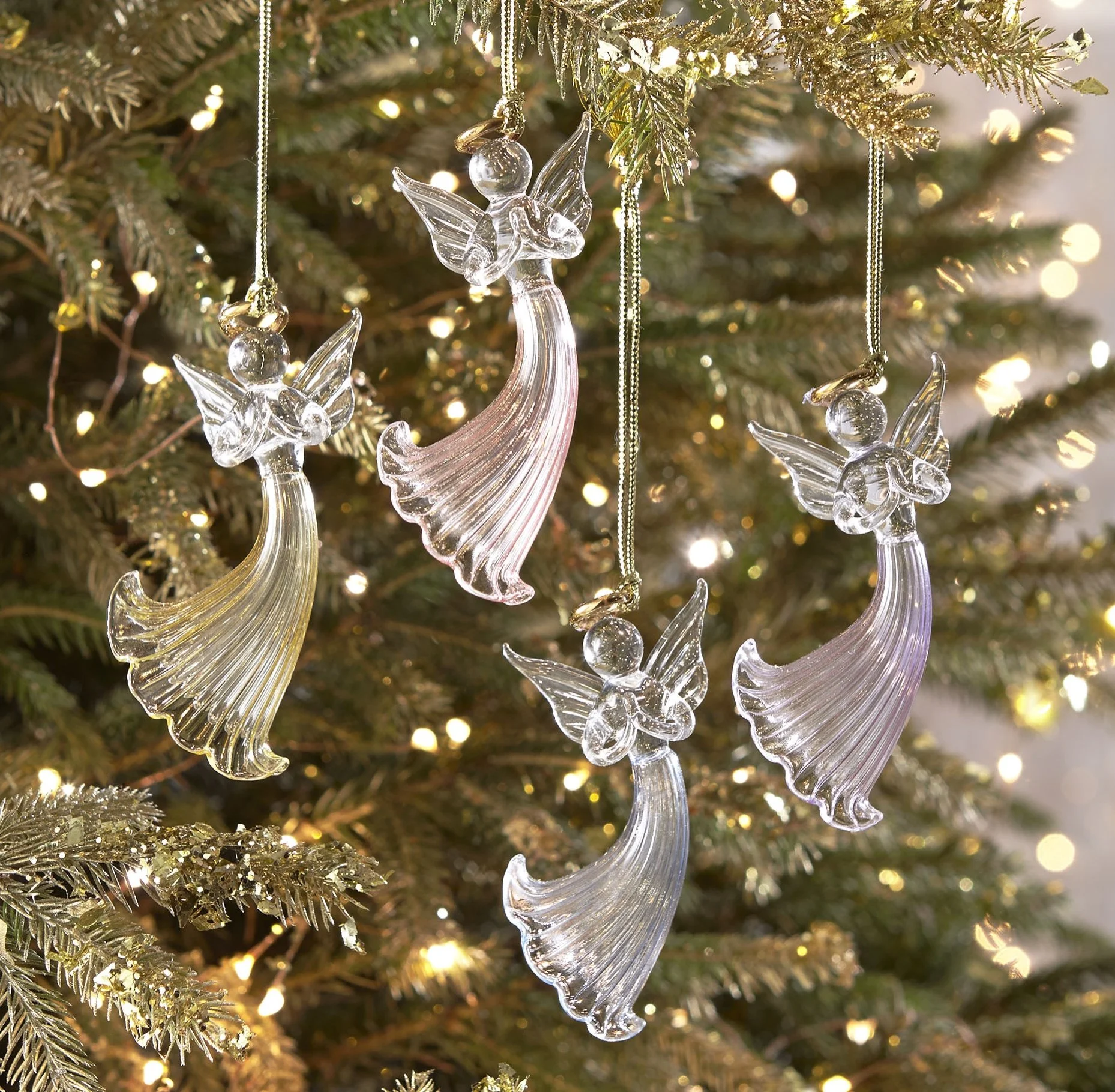 Glass angel Christmas ornaments hanging on a decorated Christmas tree with lights