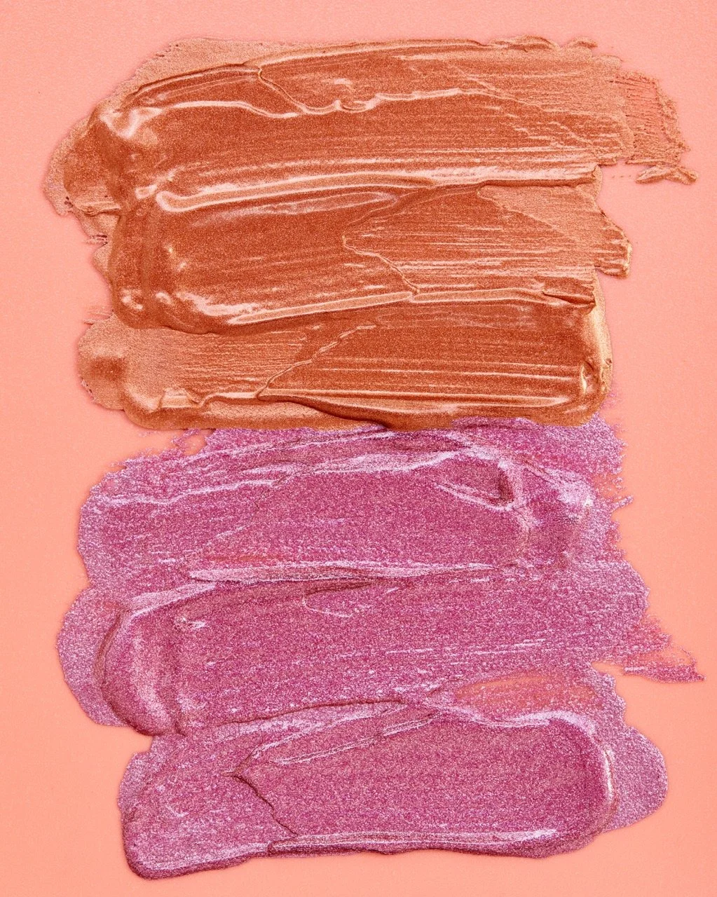 Three horizontal streaks of makeup swatches on a peach background, with the top being a shimmery tan, the middle a shimmery pink, and the bottom a darker pink with glitter.