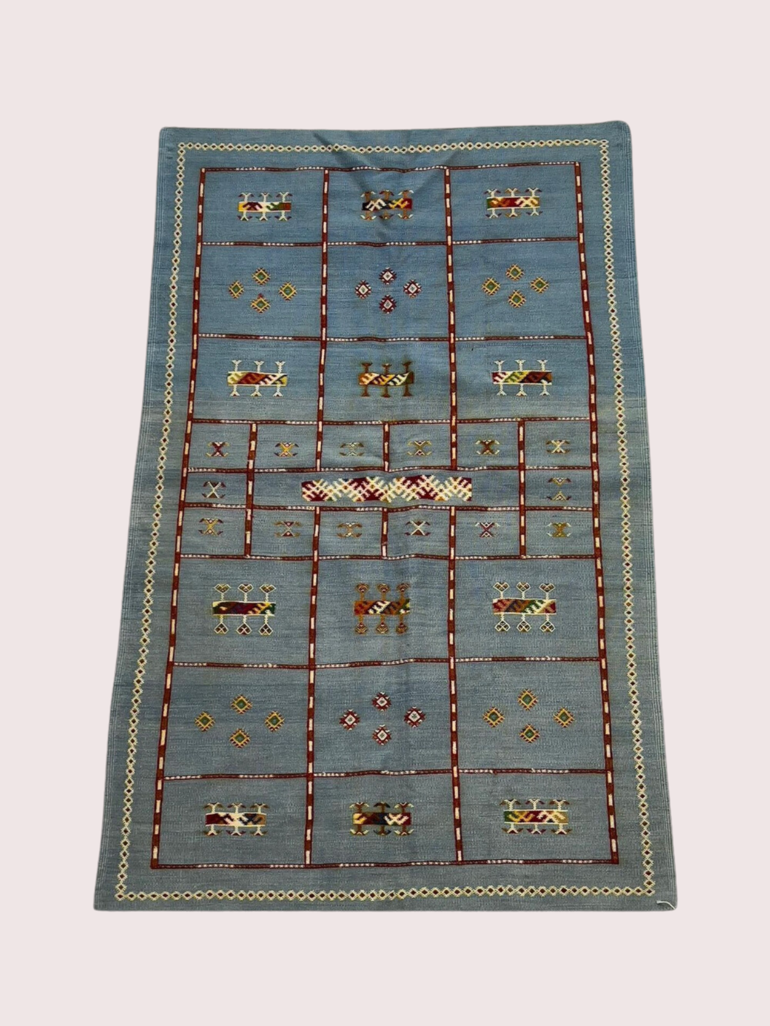 A rectangular area rug with a geometric and animal motif design, featuring a light blue background, bordered by a zigzag pattern in cream and gray, and decorated with stylized animals and geometric shapes in red, yellow, brown, and green.