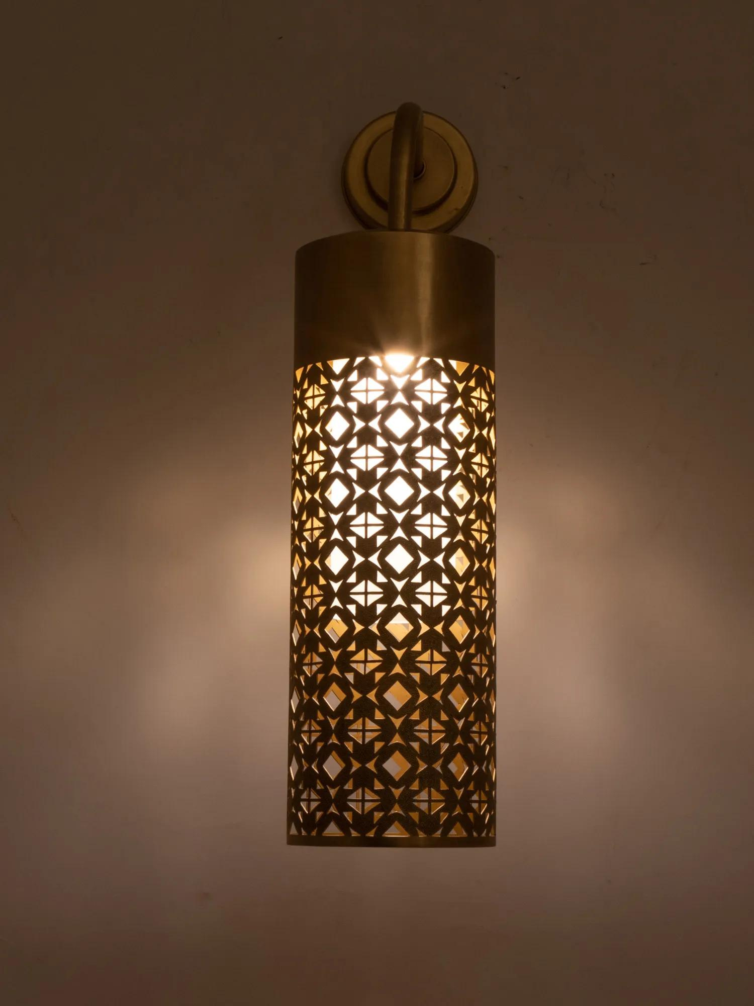 A wall-mounted pendant light with an intricate geometric cutout pattern, illuminated from within, casting patterned light on the wall.