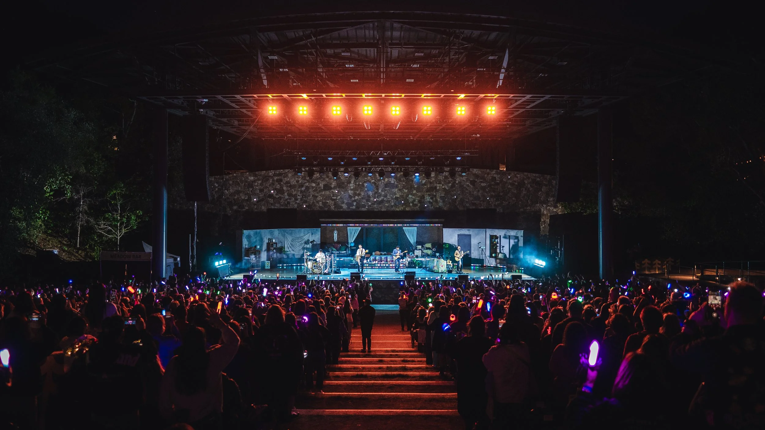 A nighttime outdoor concert with a large crowd and a band performing on stage under colorful lights.