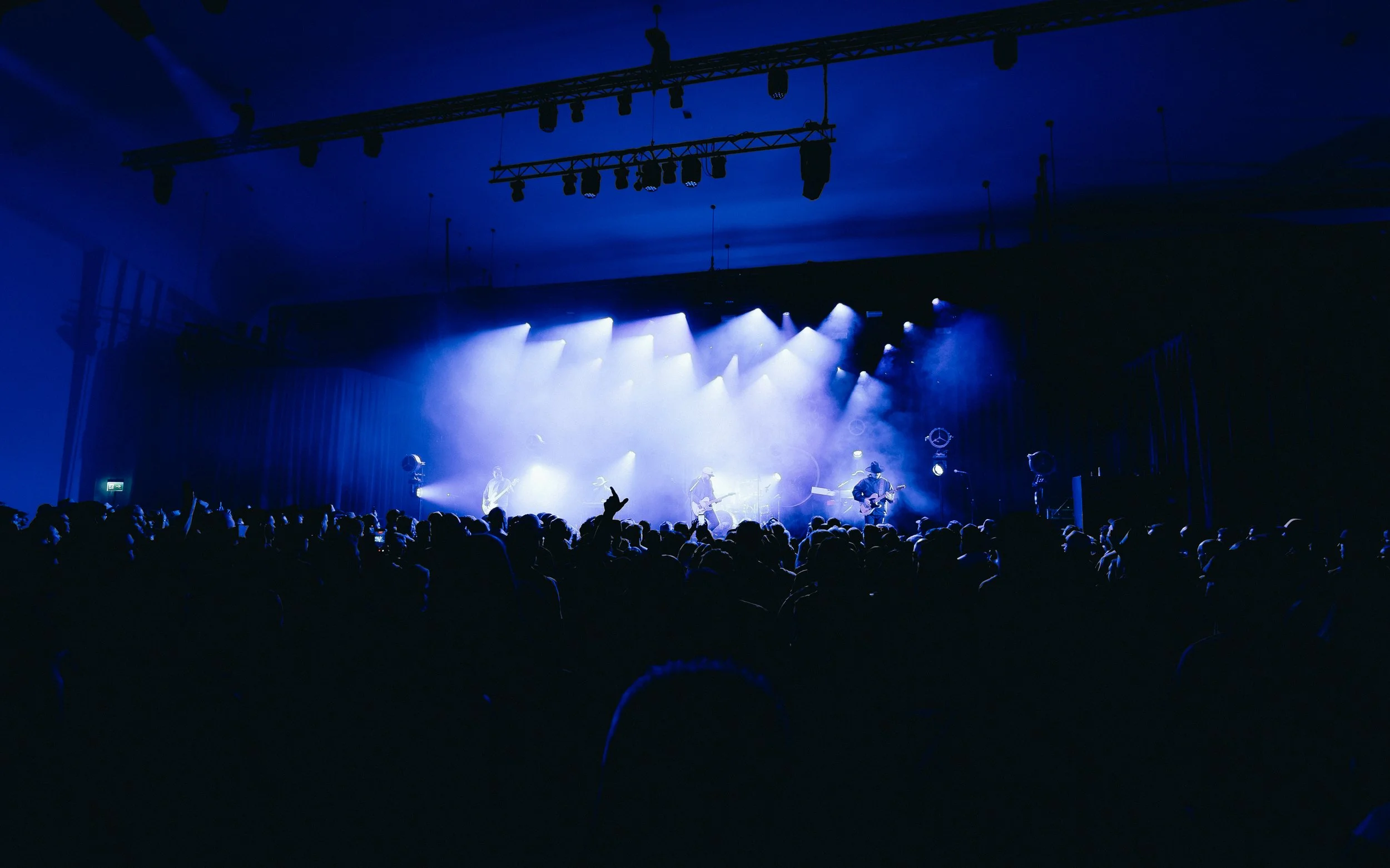 A band performing on stage with bright blue stage lighting, audience silhouettes in front.