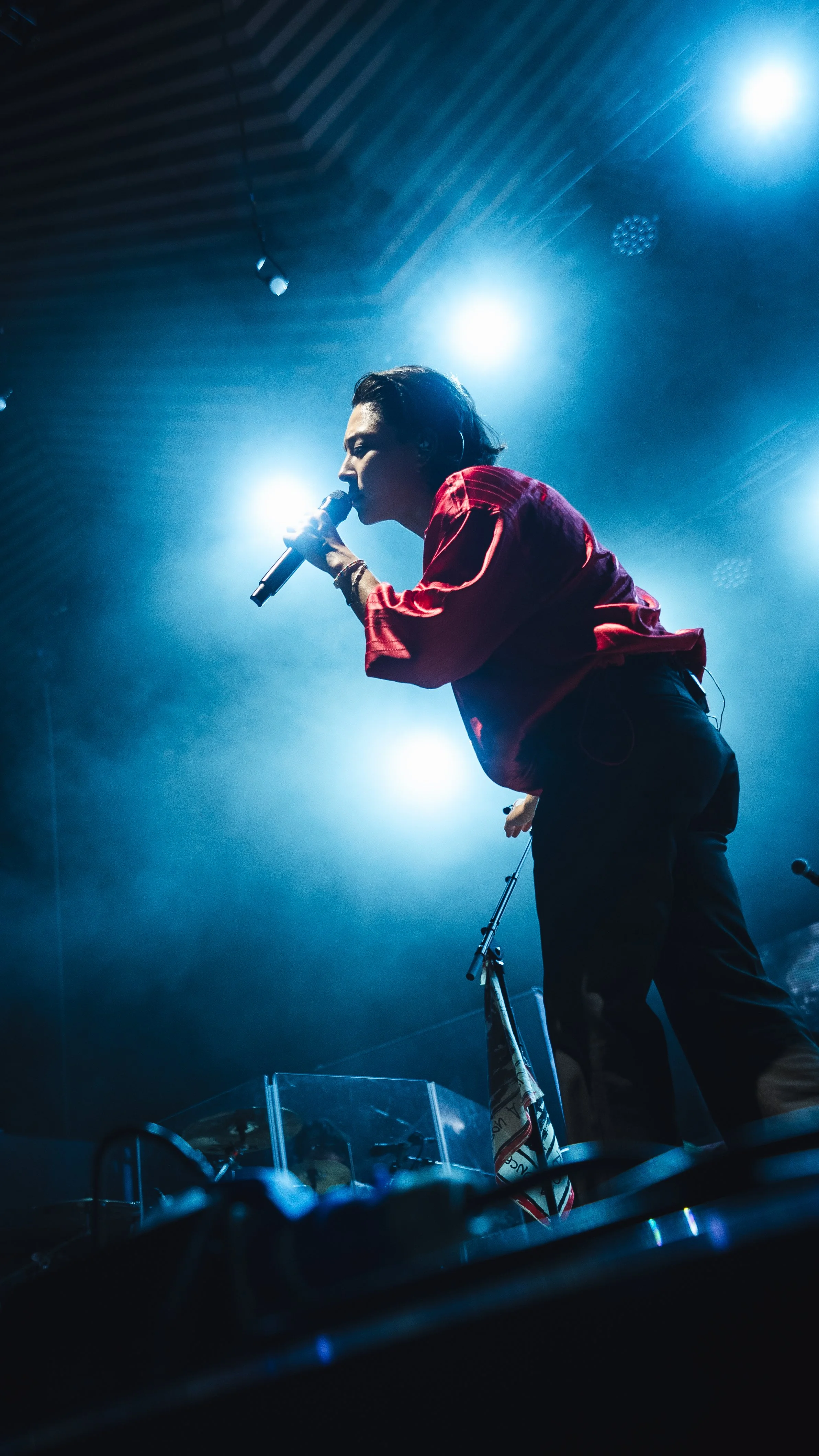 Performer singing into a microphone on stage with bright lighting and smoke effects.