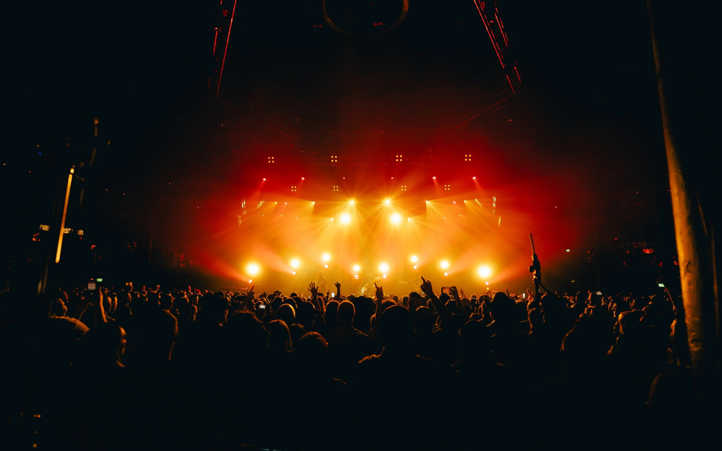 Concert scene with a crowd facing a brightly lit stage with orange and yellow lights, and a performer silhouette in the center.