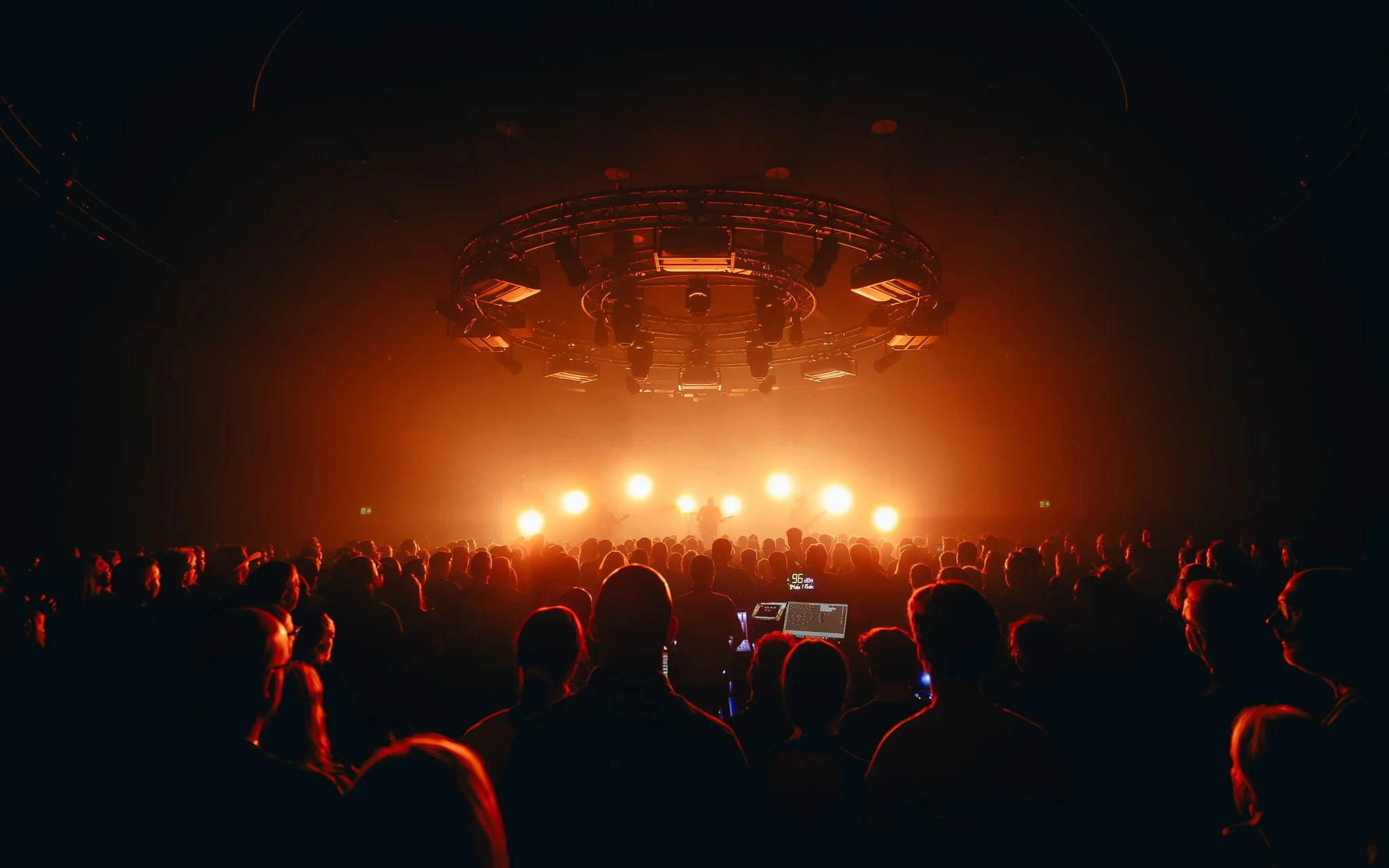 Audience watching a concert or performance with bright orange lights on stage in a dark venue.