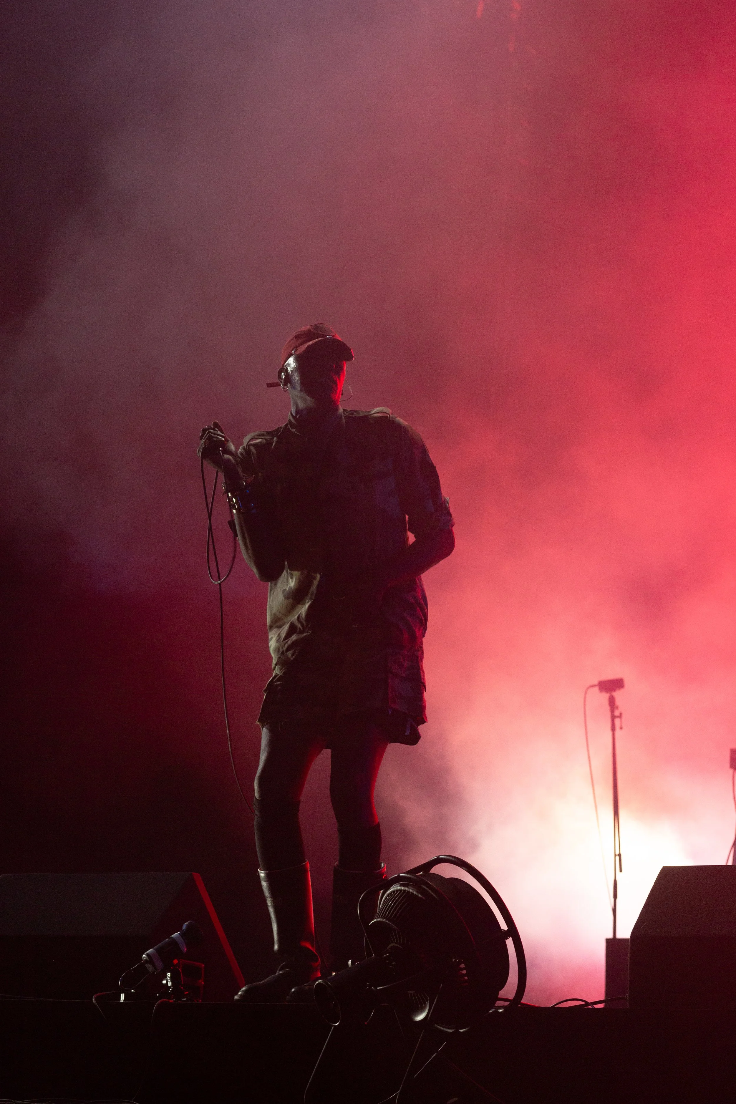 Silhouette of a performer holding a microphone on stage with red lighting and fog.