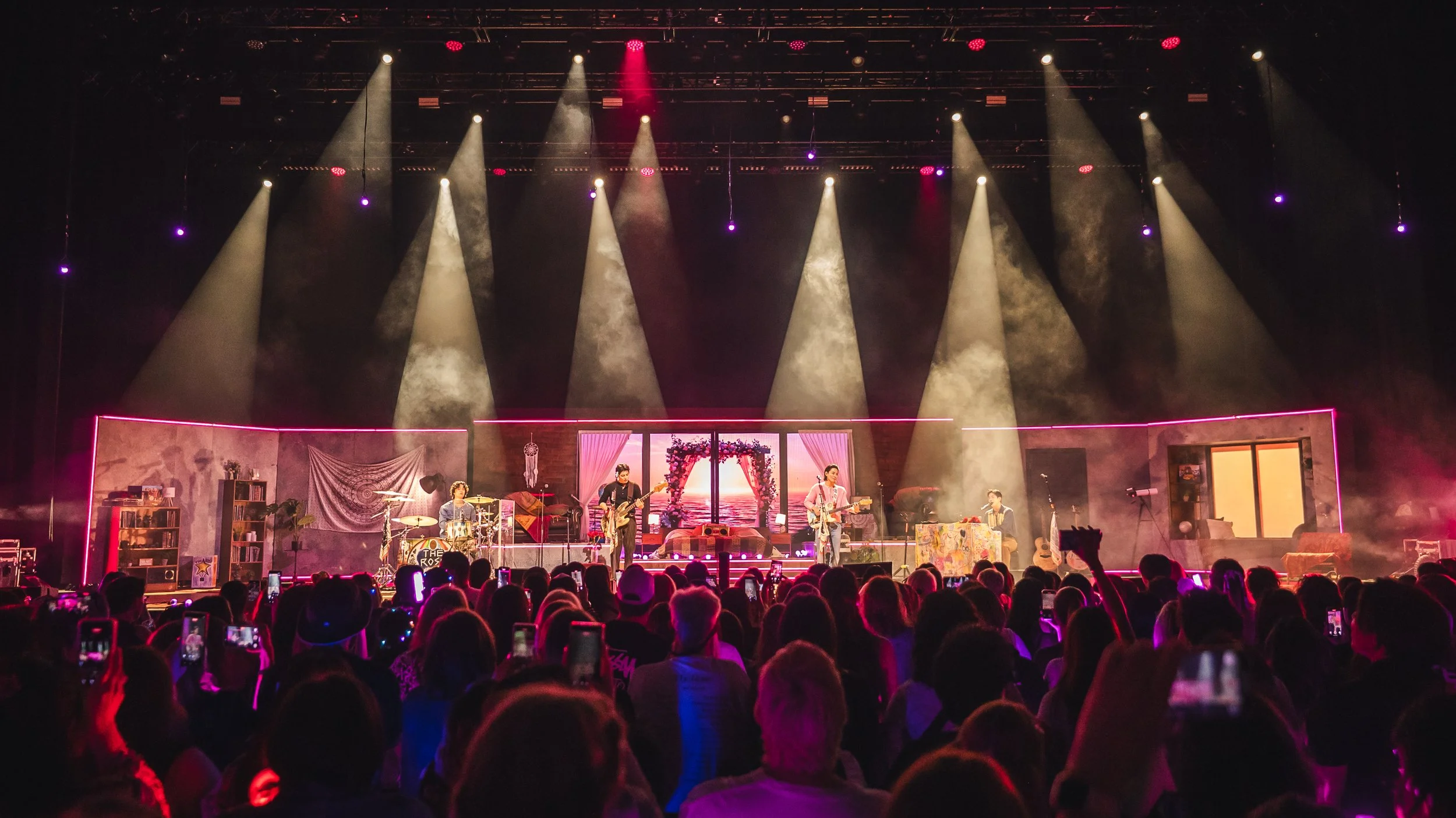 A live concert capturing a band performing on stage with colorful lighting and audience holding up phones