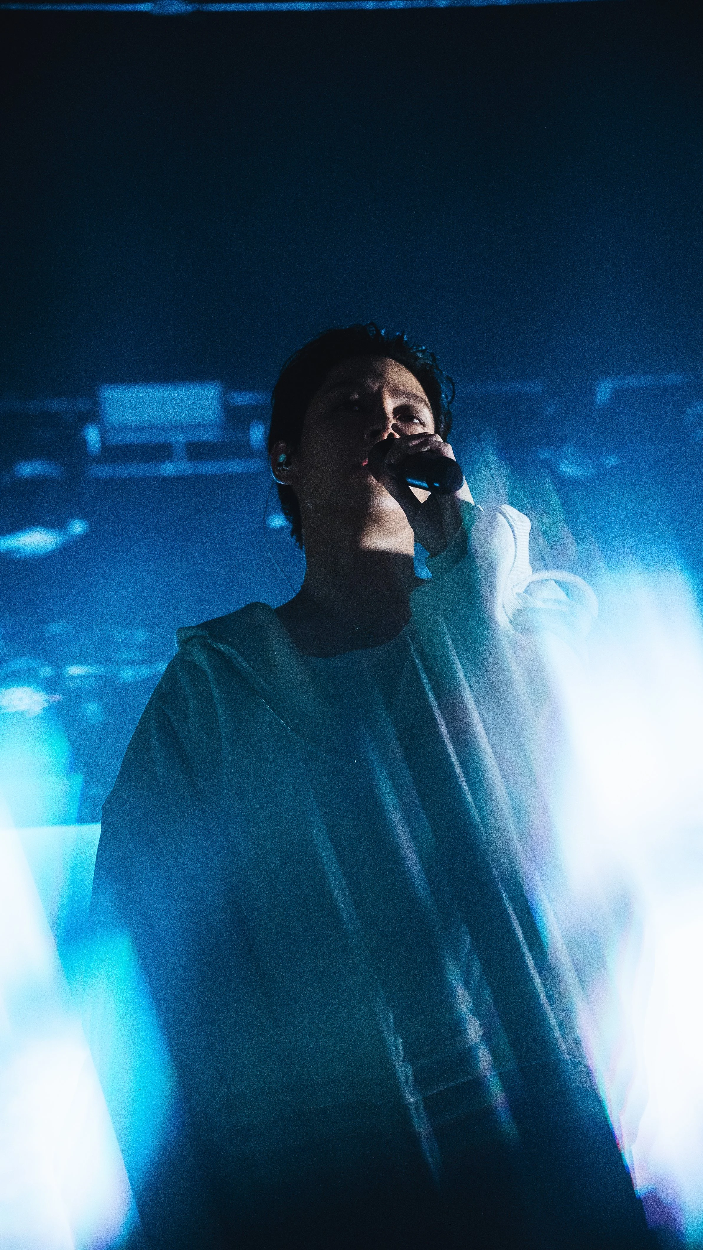 A singer performing on stage, holding a microphone, with stage lighting creating a silhouette effect.