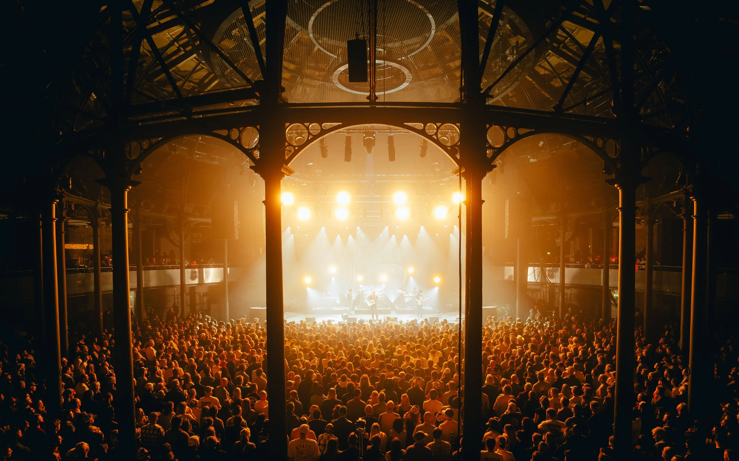 Large crowd watching a band perform on stage in a concert hall with bright lights and ornate architectural details.