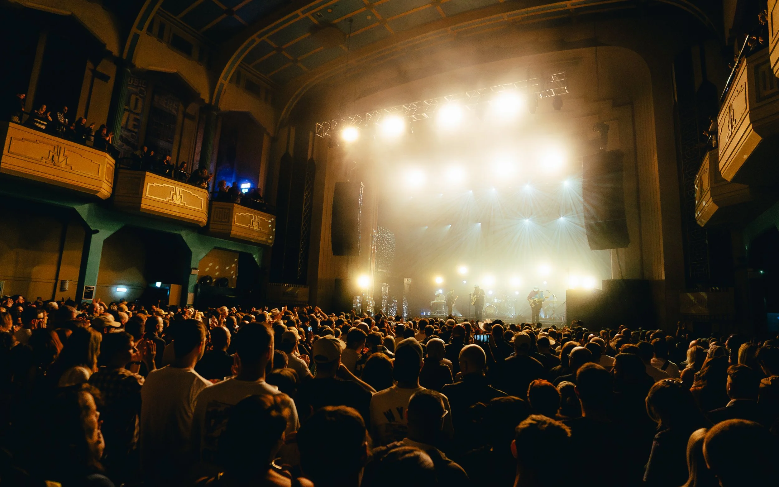 Crowd watching a live music concert in an ornate theater with a brightly lit stage.