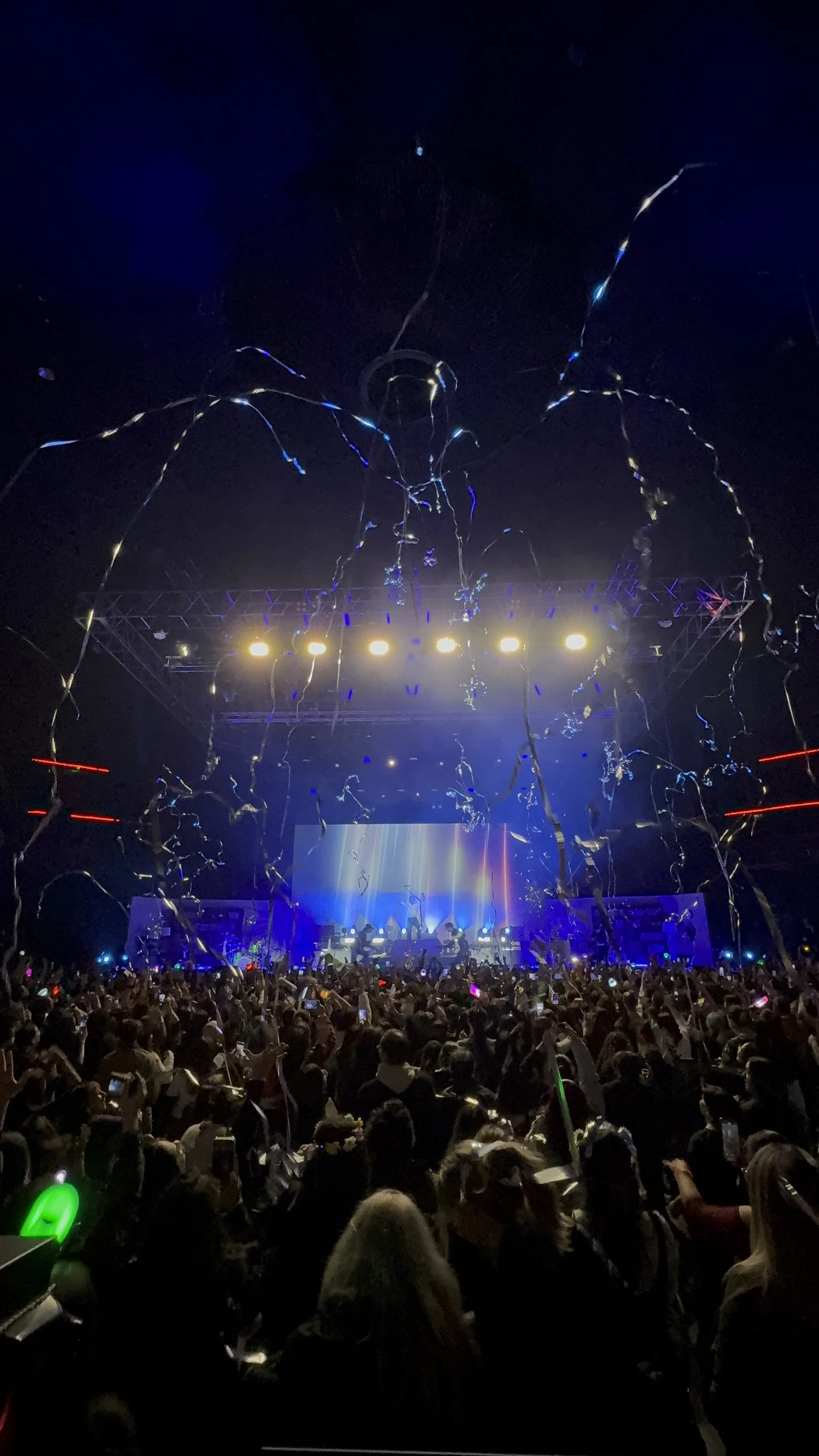 Concert crowd with stage lights and streamers in the air.