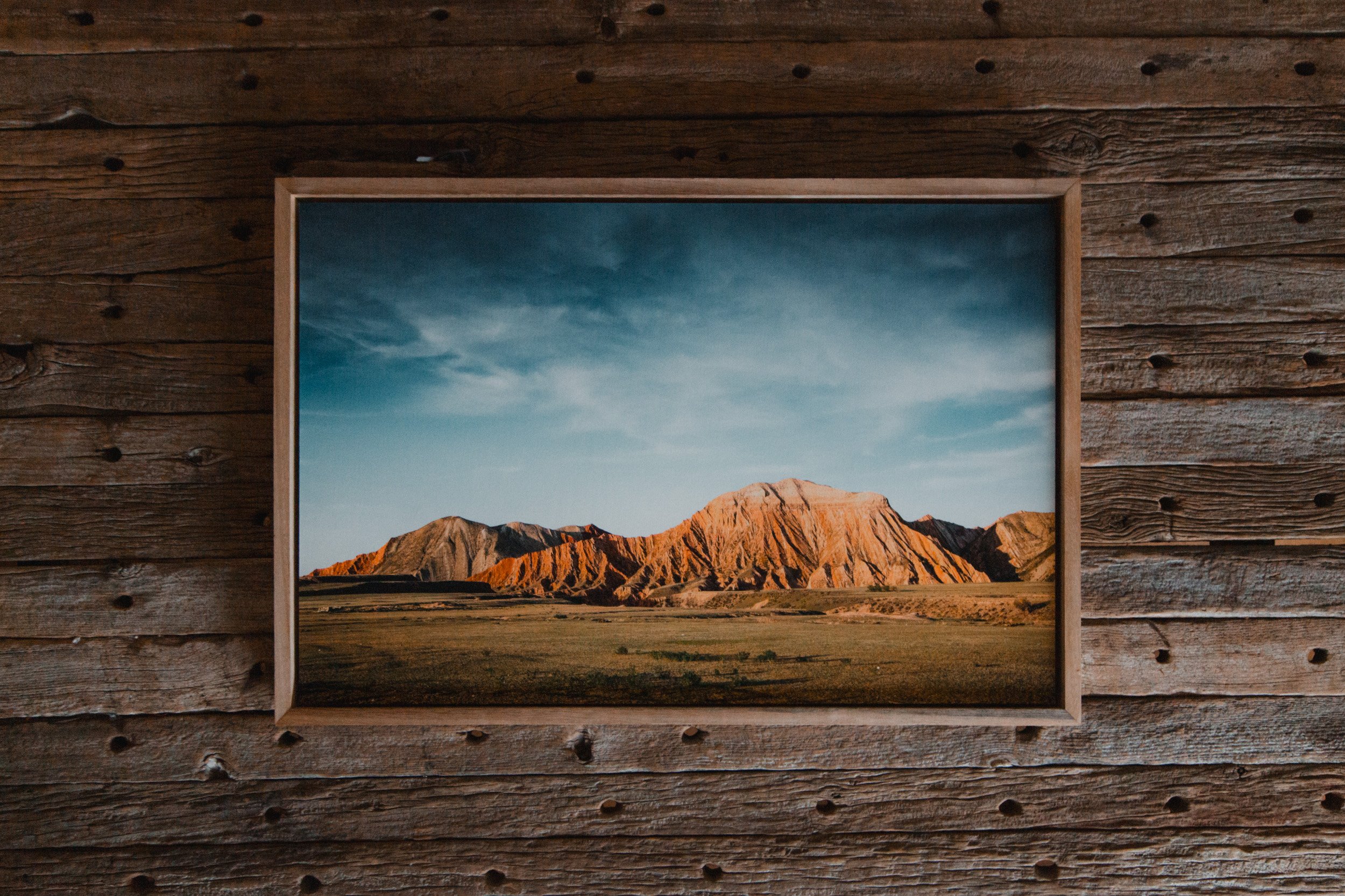 Framed landscape photograph of a mountain range with blue sky, mounted on a wooden wall.
