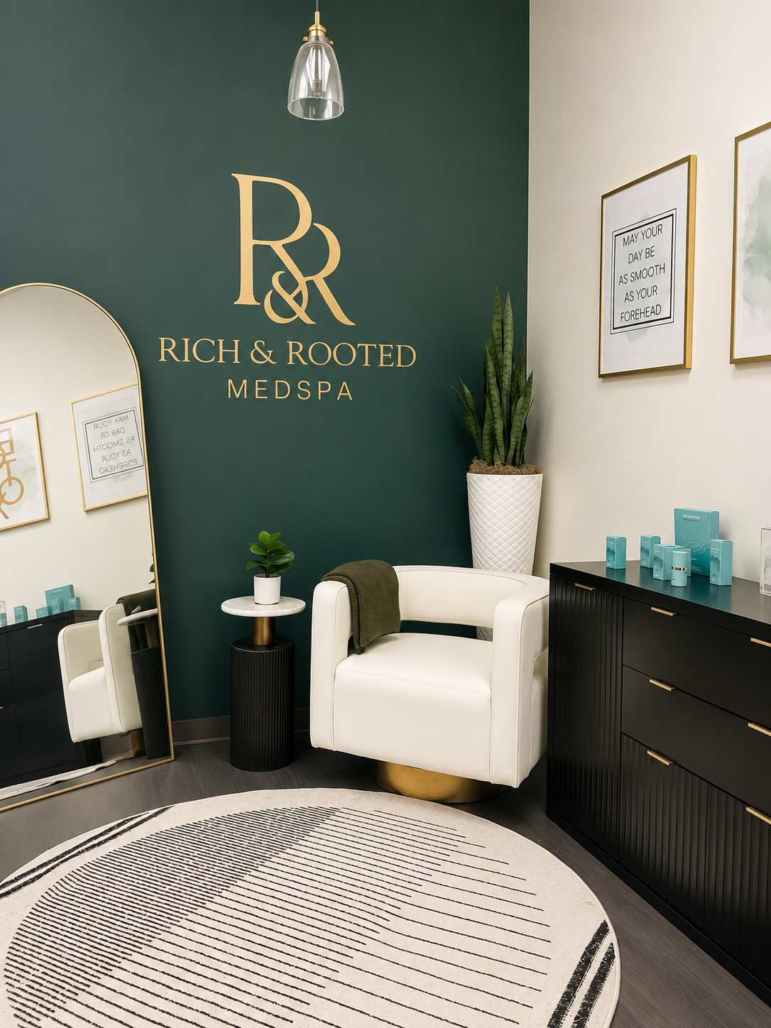 Luxury receptionist area at Rich & Rooted Medspa in Katy, Texas, featuring the emerald brand wall, gold logo, and modern aesthetic workspace