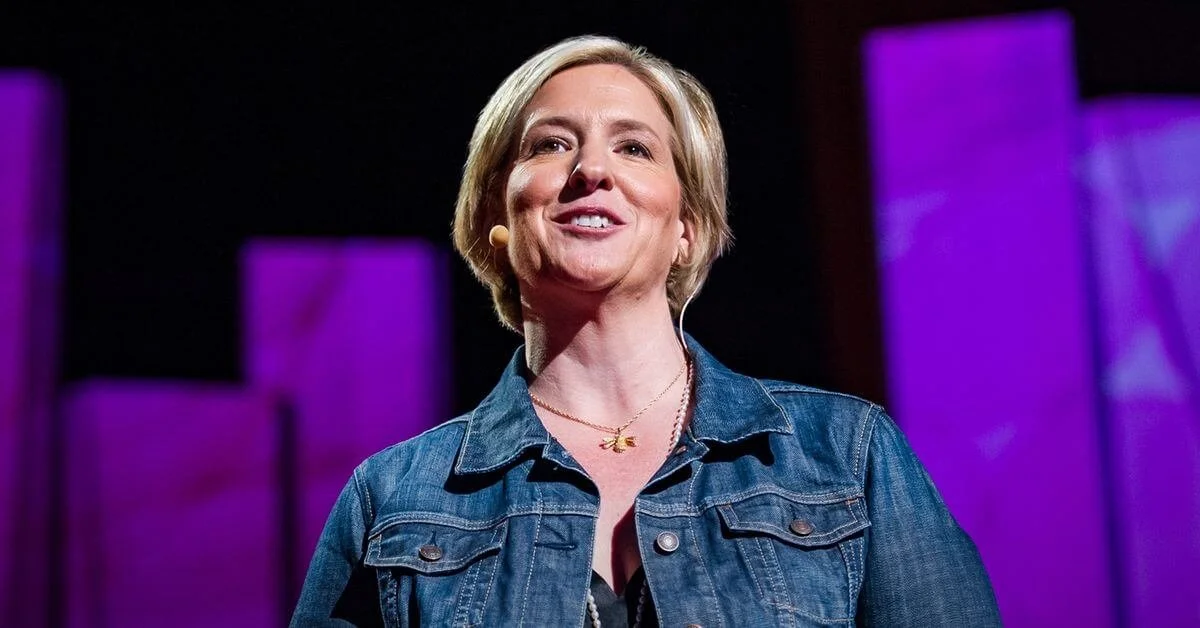 Brene Brown, an expert in connection, in a denim jacket speaking at a stage with purple background lighting providing fantastic communication recommendations for professionals.