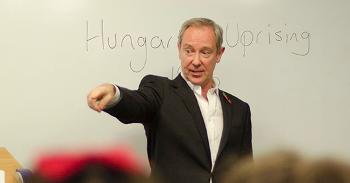 A man in a suit and white shirt pointing during a presentation in front of a whiteboard with the words "Hunger Uprising" written on it