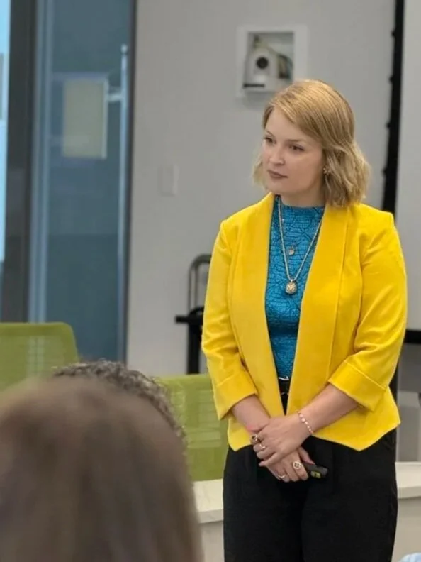 Sydney Parriott in a yellow blazer holding a presentation clicker while delivering professional communication training and public speaking coaching.