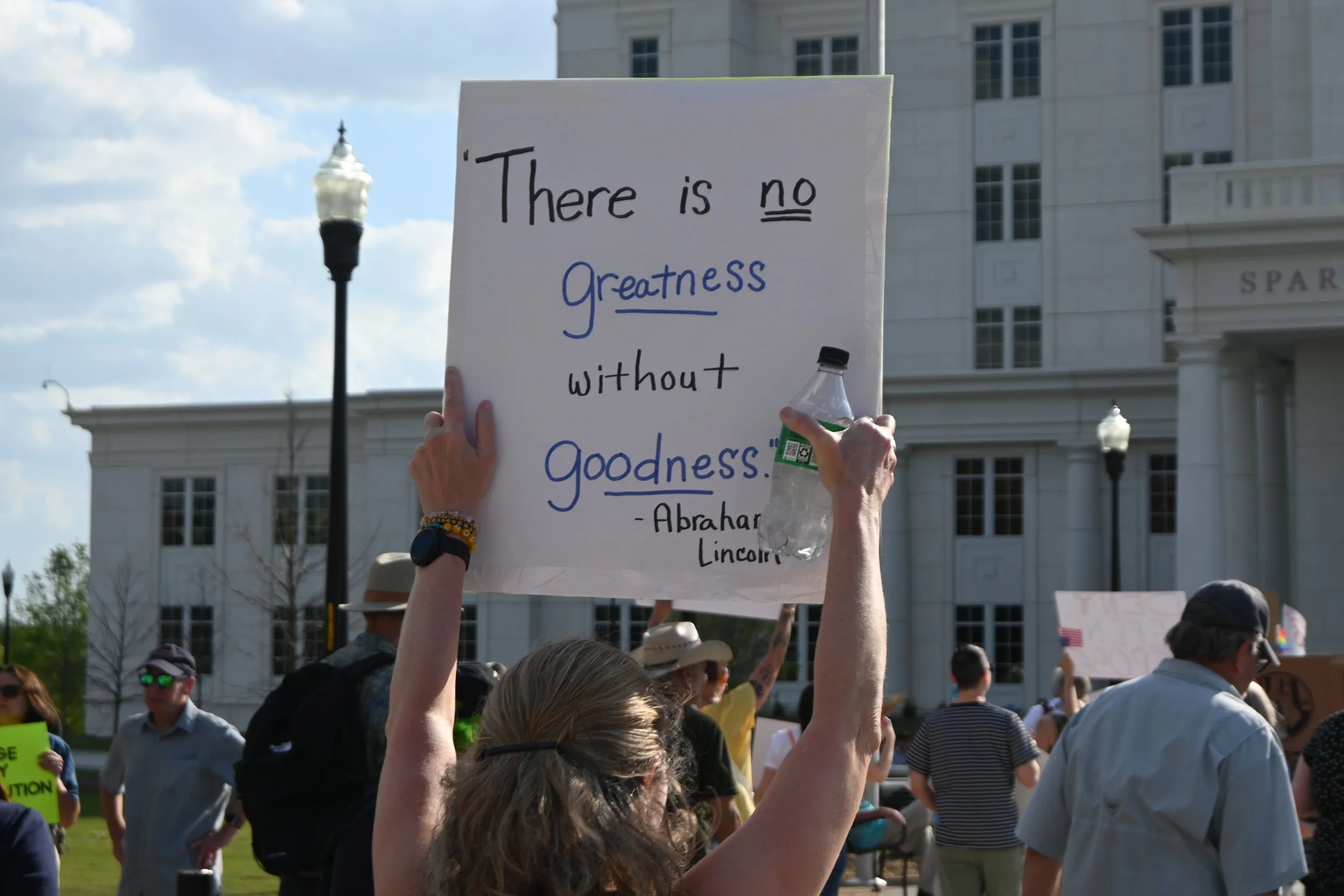 A person holding a sign with a quote by Abraham Lincoln in a crowd of protesters outdoors in front of a government building.